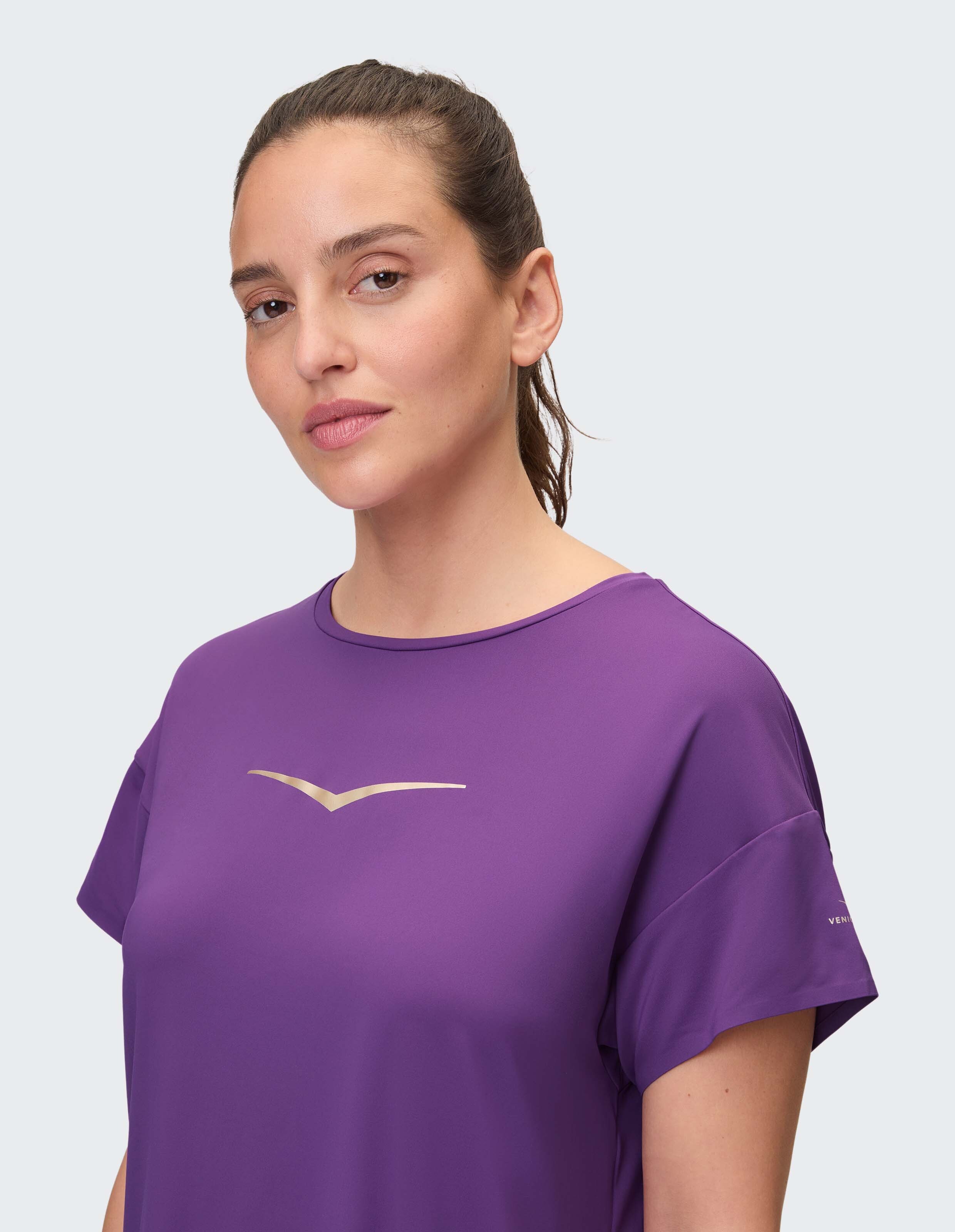 Frau trägt ein gemütliches lilafarbenes Freizeit-T-Shirt mit metallischem Logo auf hellem Hintergrund.