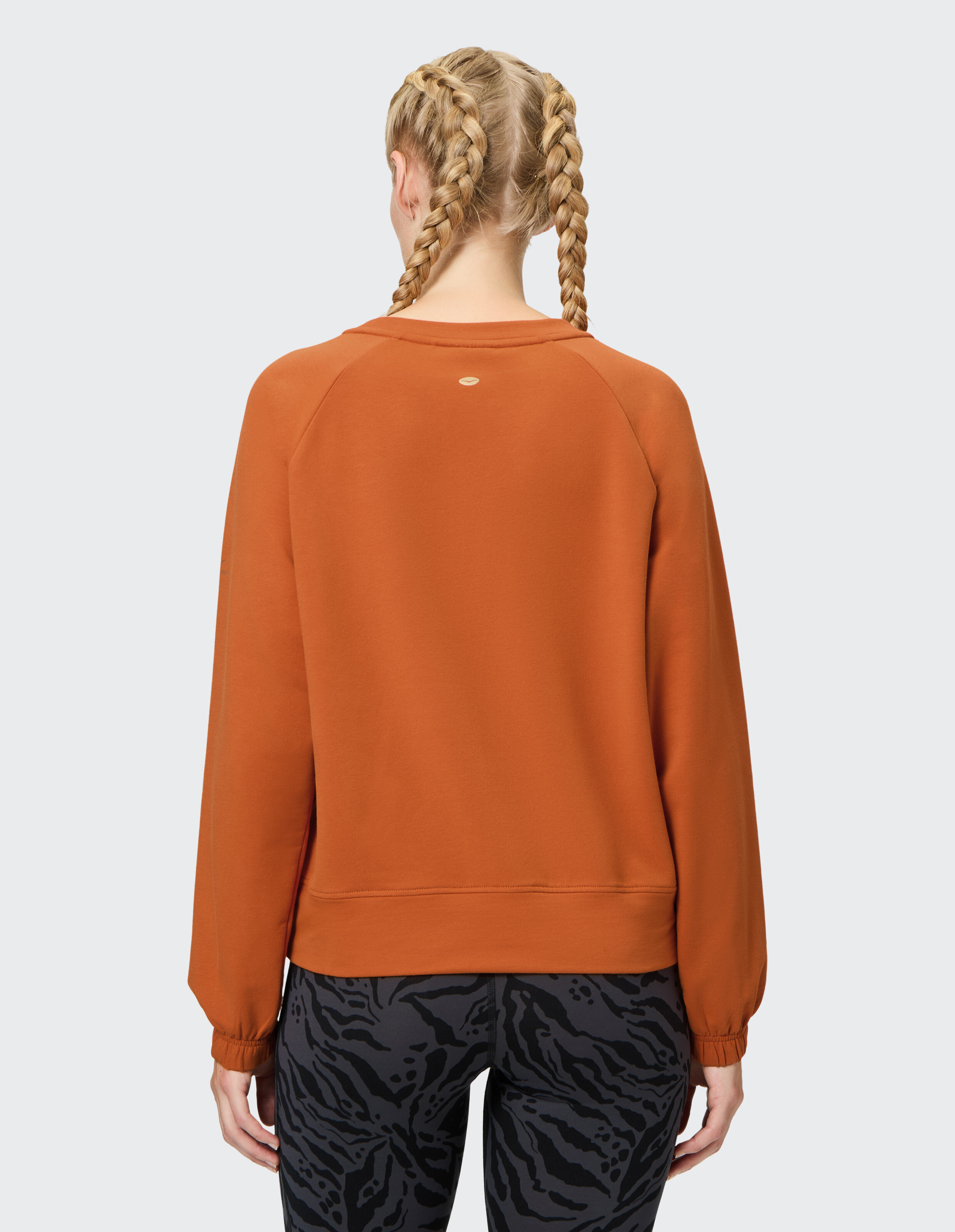 Rückansicht einer Frau in einem orangefarbenen Sweatshirt und gemusterten Leggings.