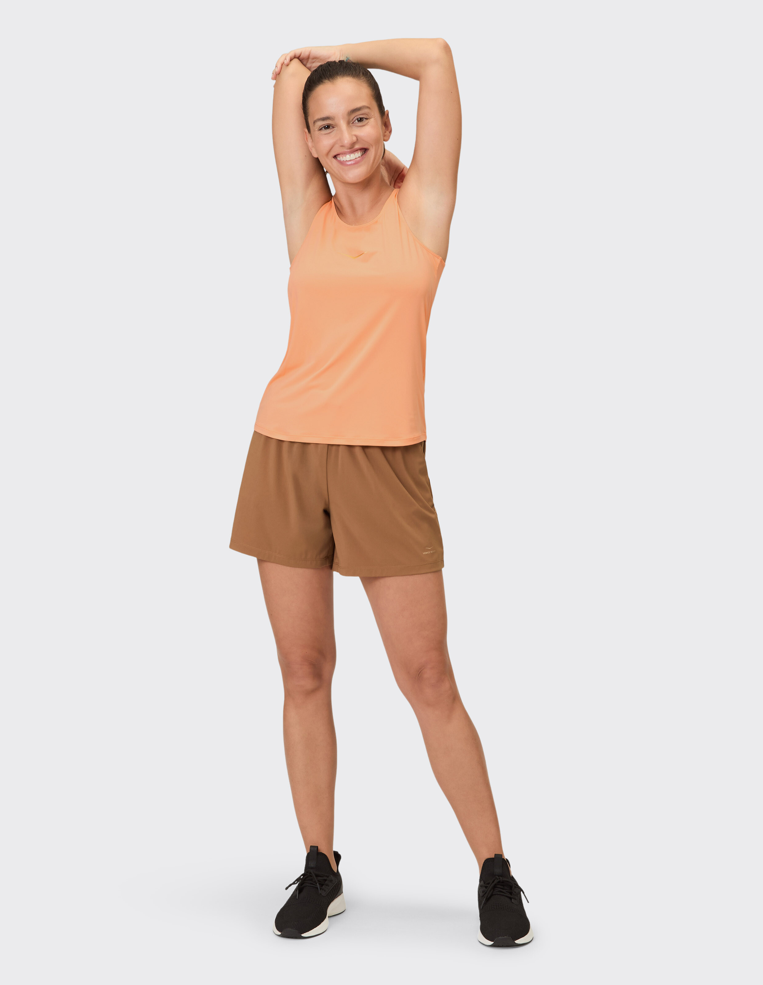 Lächelnde Frau in einem orangefarbenen Tanktop und braunen Shorts, perfekt für Freizeitkleidung.