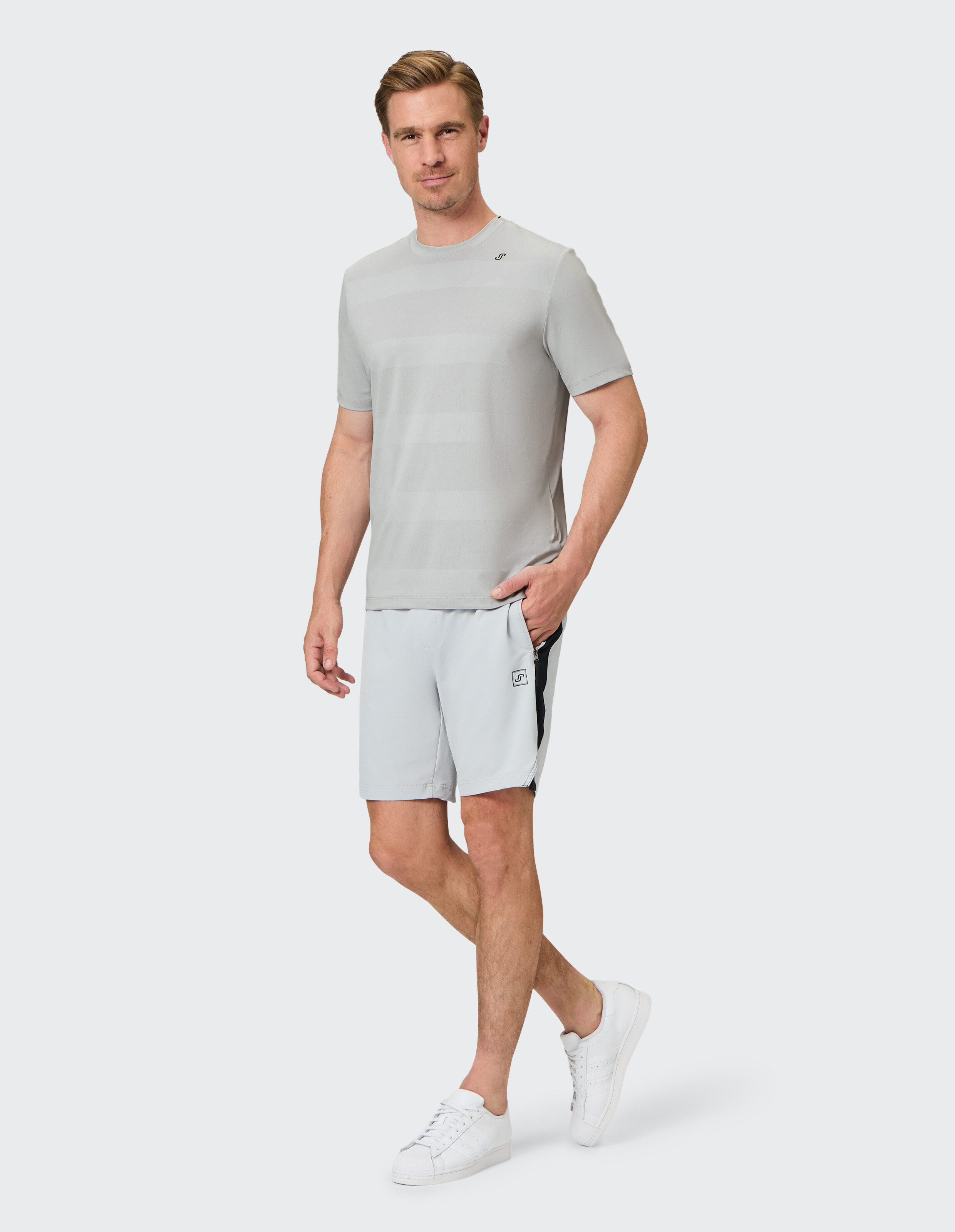 Mann trägt ein hellgrau gestreiftes T-Shirt und passende Freizeitshorts mit weißen Turnschuhen.