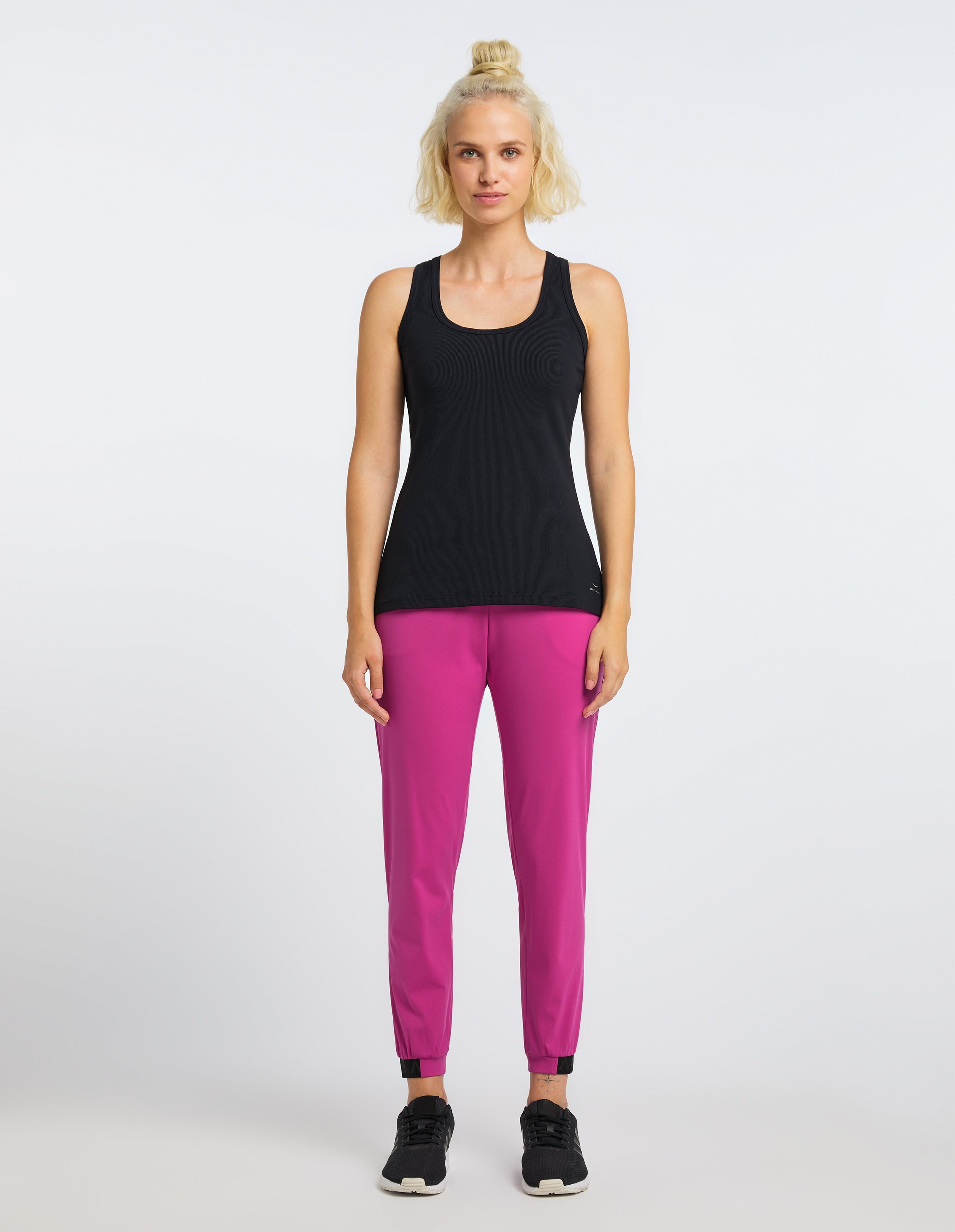 Frau trägt das schwarze Venice Beach Tanktop Brenda mit rosa Jogginghosen für einen lässigen Stil.