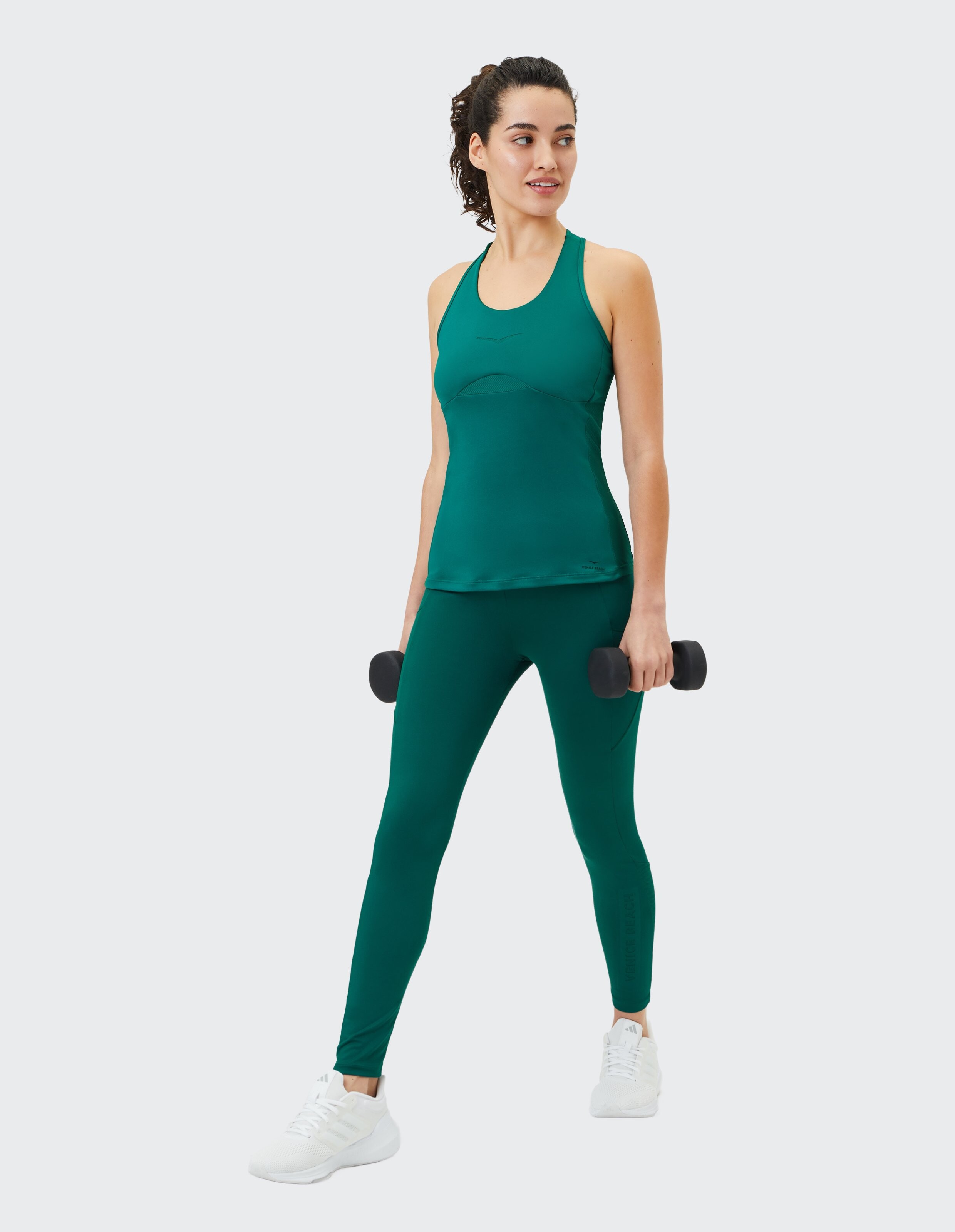 Frau in einem grünen Tanktop und Leggings hält Hanteln für ein Training.