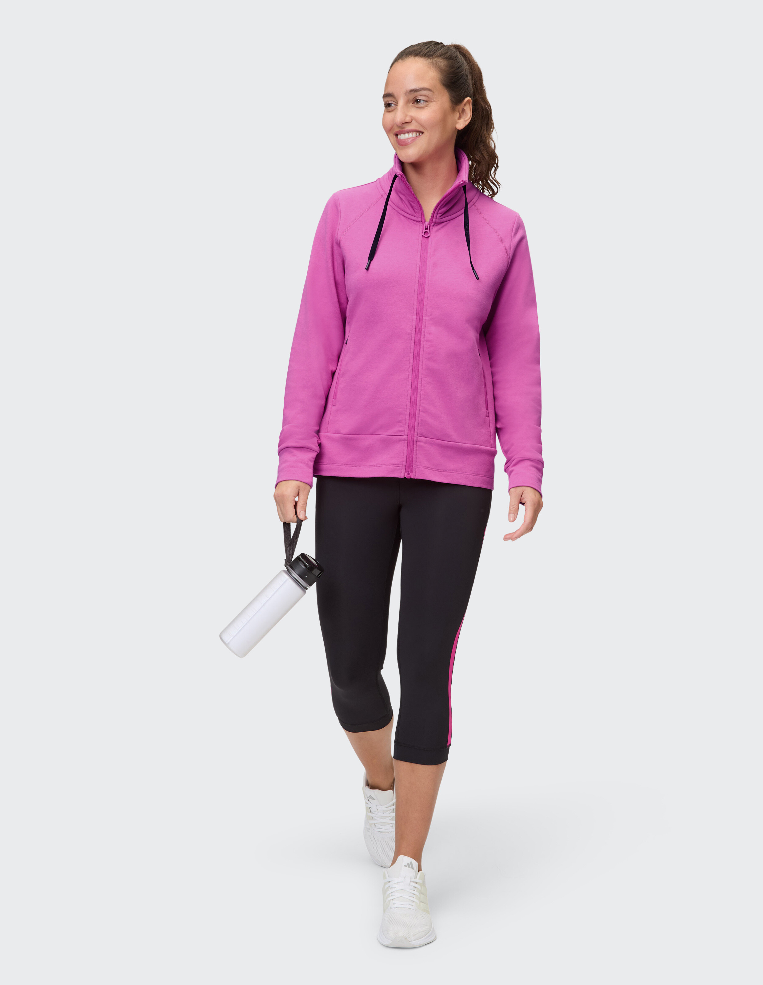 Frau trägt einen rosa Kapuzenpullover mit Reißverschluss und schwarze Leggings für einen lässigen, sportlichen Stil.