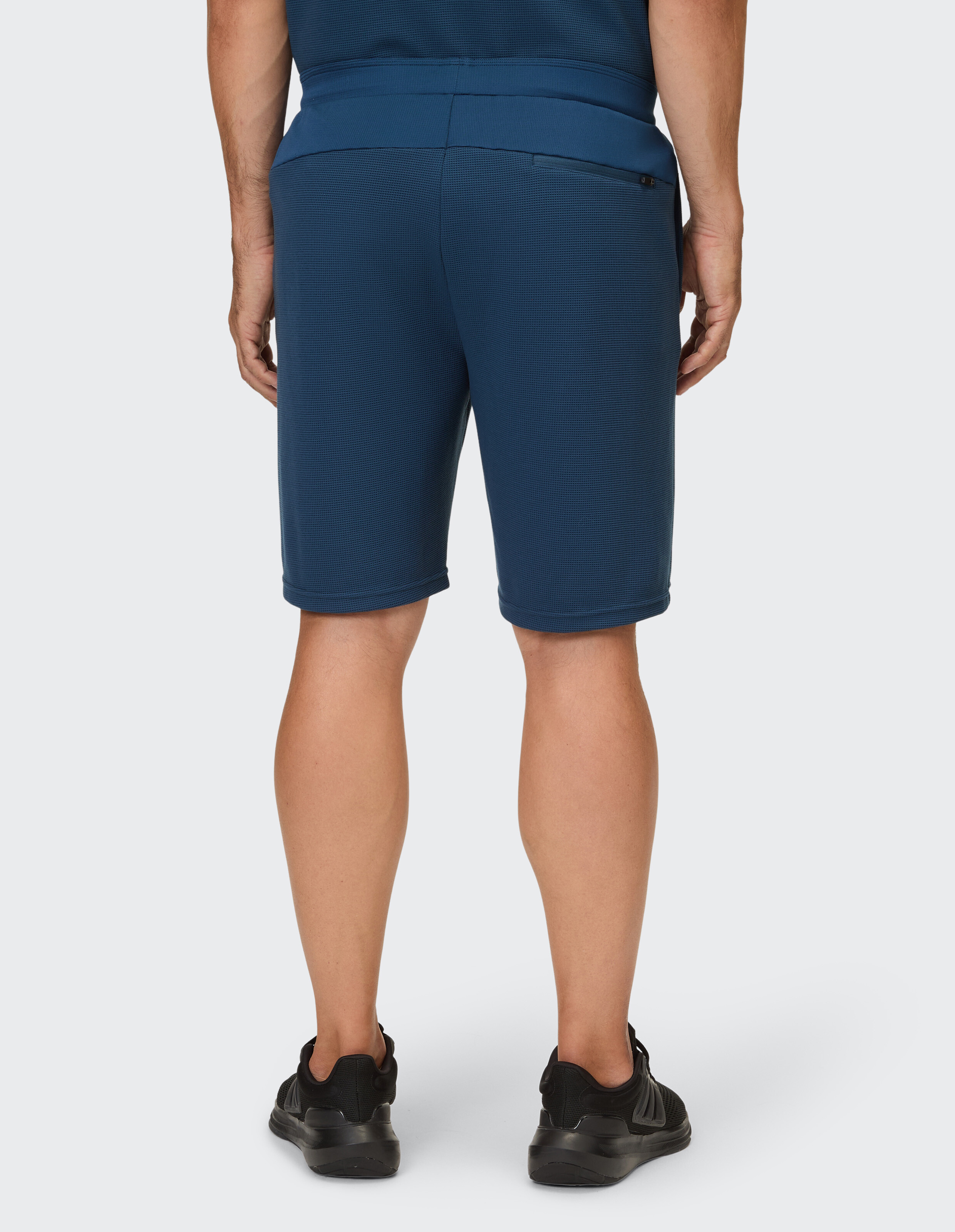 Eine Person trägt eine dunkelblaue, kurze Hose mit Waffelstruktur und schwarzen Turnschuhen.