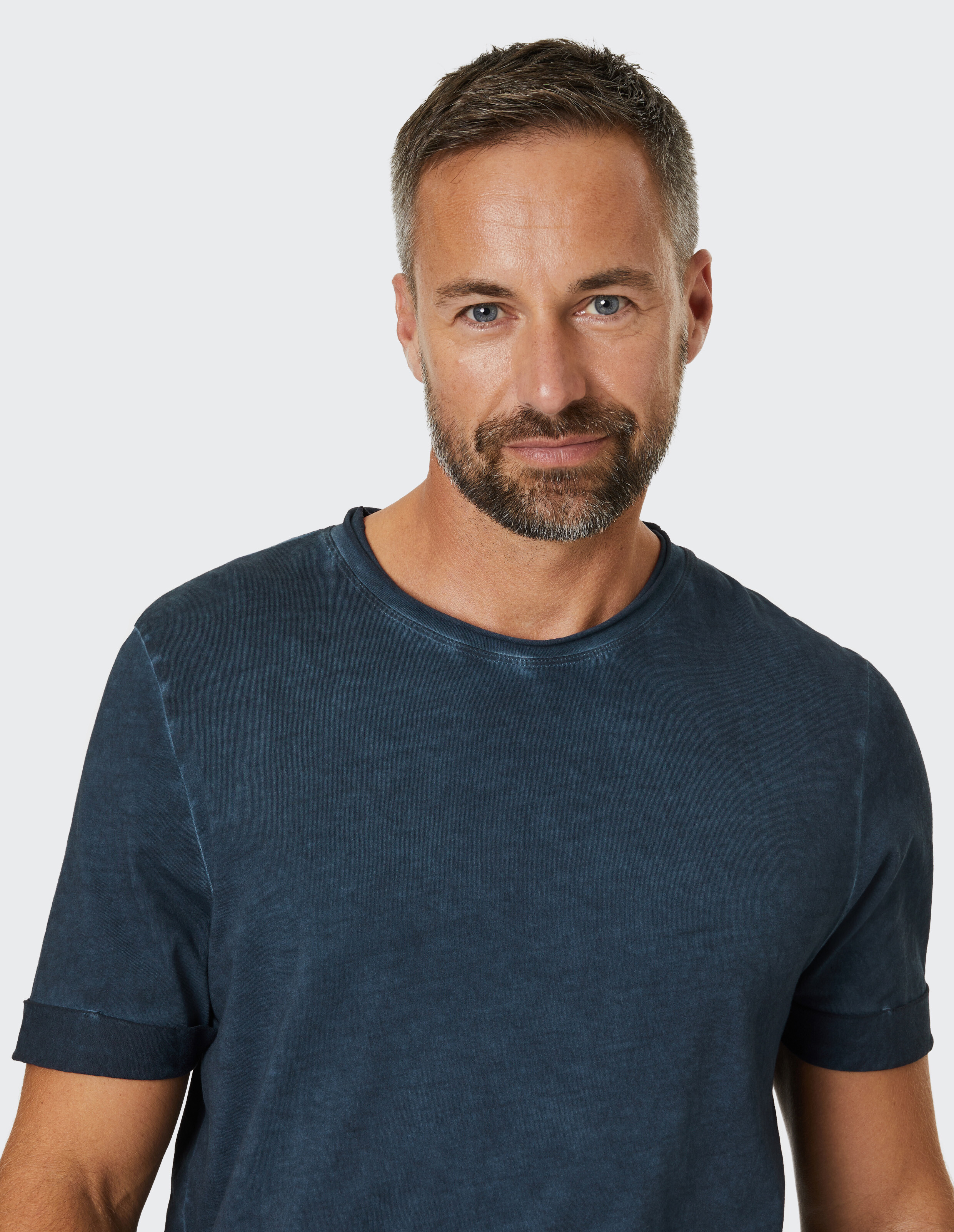 Mann trägt ein lässiges dunkelblaues T-Shirt mit hochgekrempelten Ärmeln für einen gemütlichen, stilvollen Look.