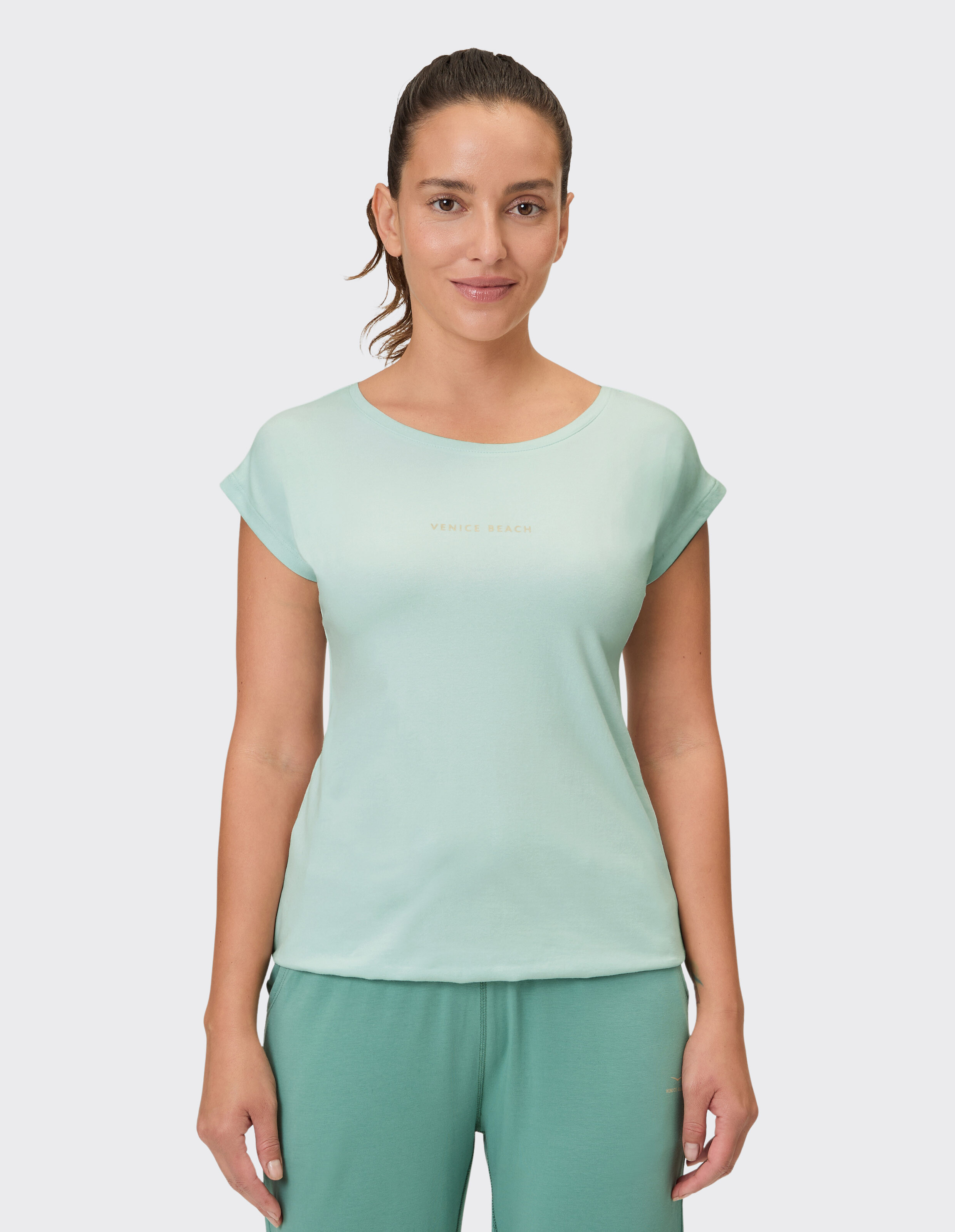 Frau trägt ein hellgrünes Freizeit-T-Shirt mit Venice Beach-Logo als Loungewear.