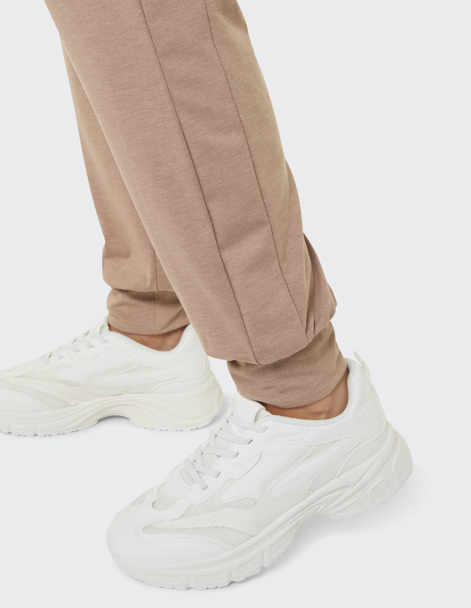 Nahaufnahme einer beigen Jogginghose gepaart mit weißen sportlichen Sneakers, ideal für Freizeitkleidung.