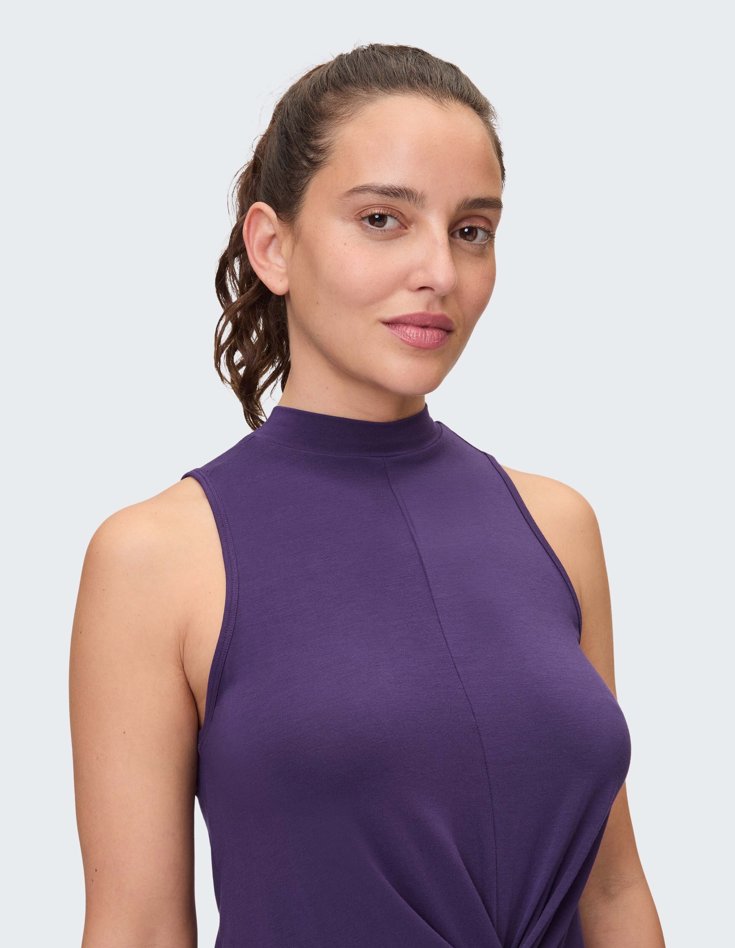 Das Model trägt ein ärmelloses lila Oberteil mit hohem Ausschnitt und zeigt damit einen lässigen Stil.