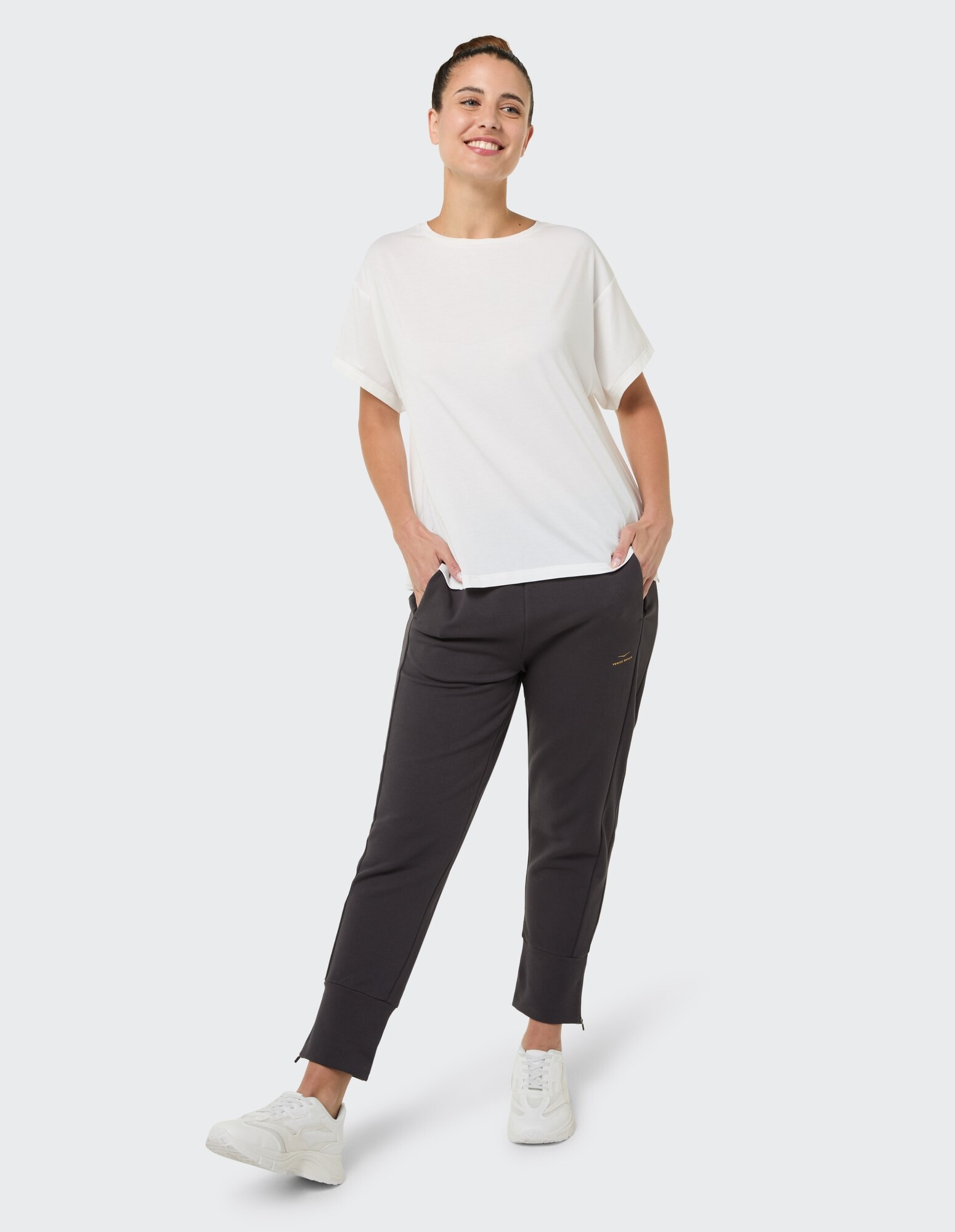 Frau in einem weißen, entspannten T-Shirt und dunklen Jogginghosen, gestylt für lässigen Komfort.