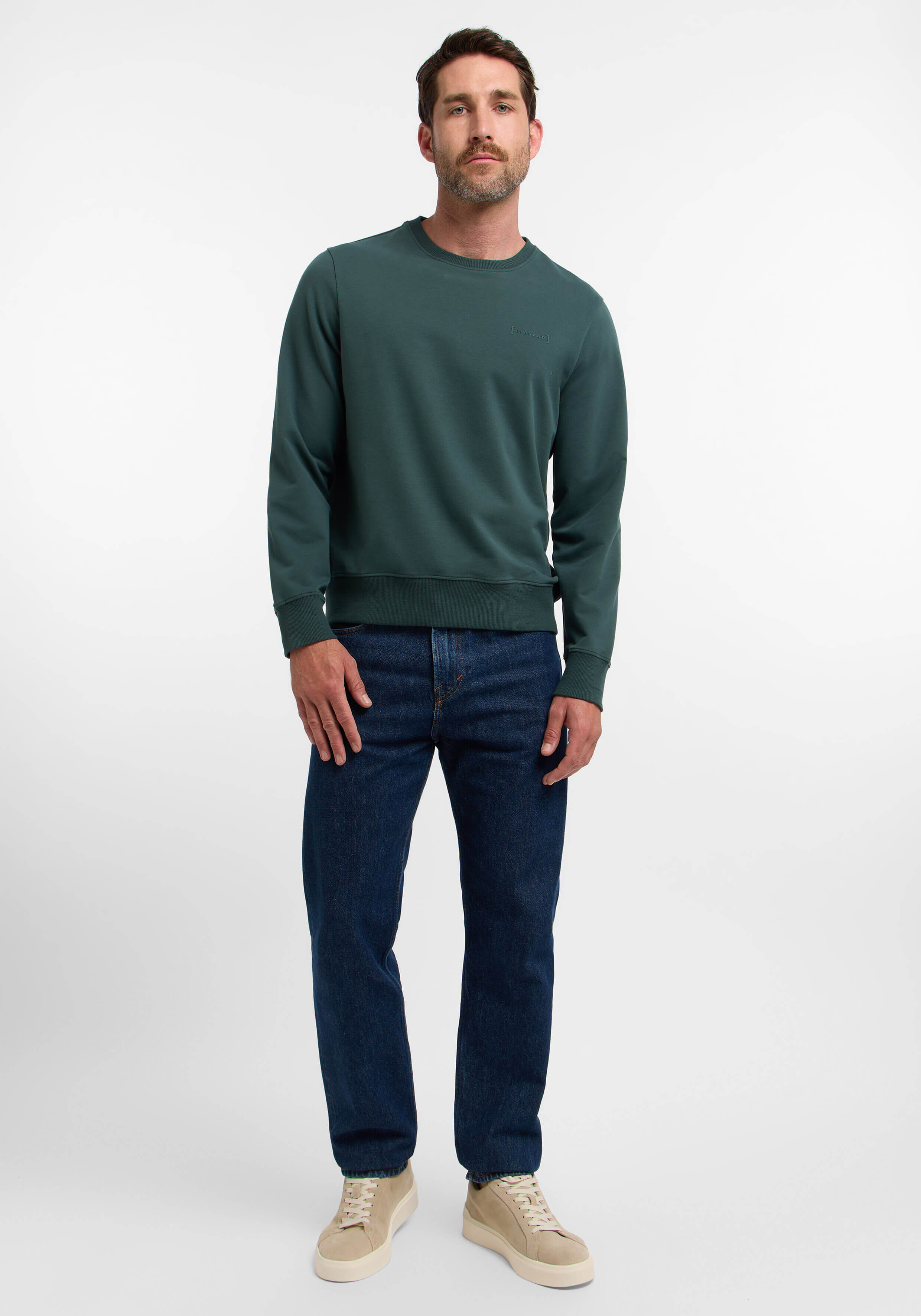 Mann trägt ein grünes Sweatshirt und blaue Jeans, lässig gestylt.