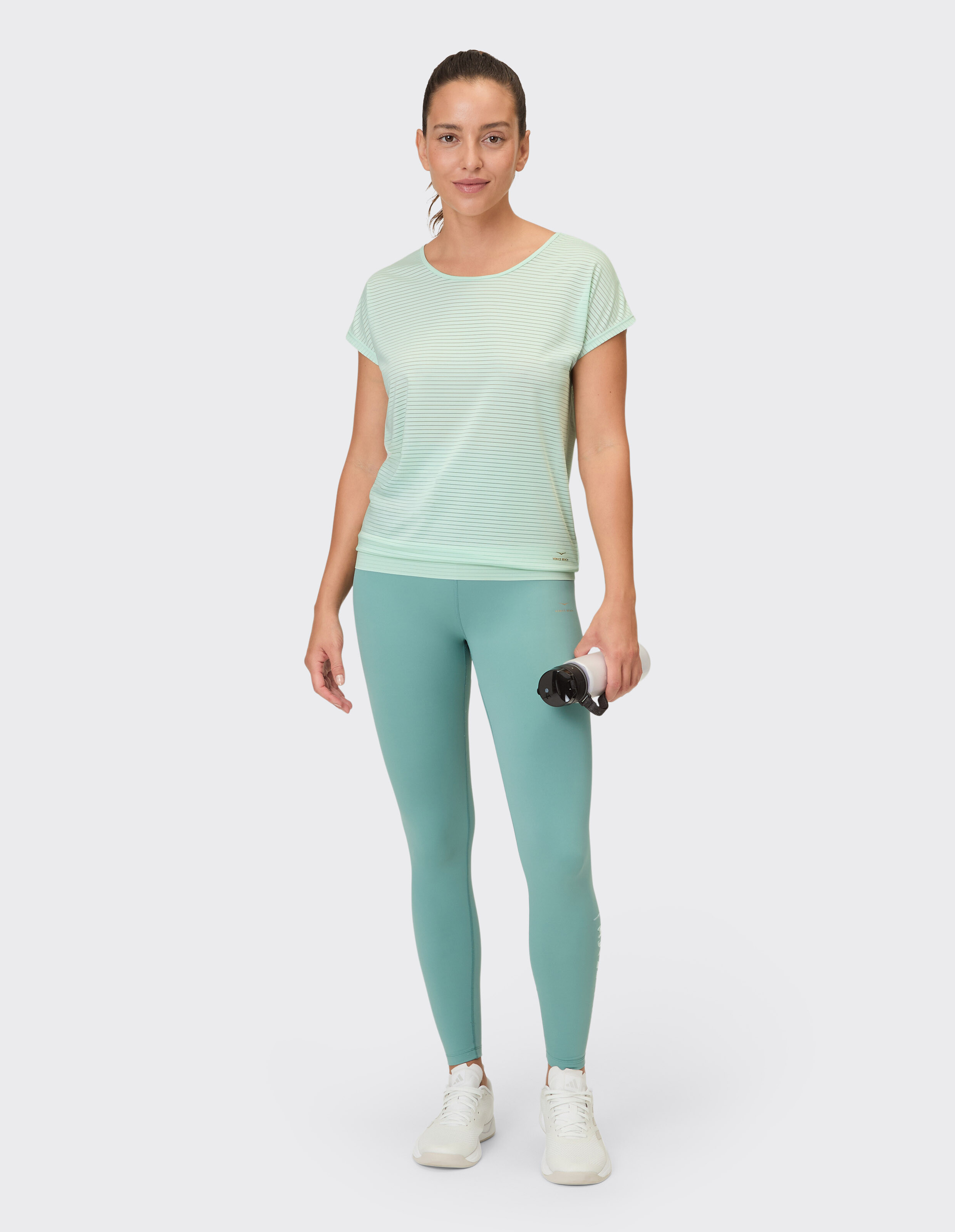 Frau trägt ein hellgrün gestreiftes T-Shirt und blaugrüne Leggings für lässige Aktivkleidung.