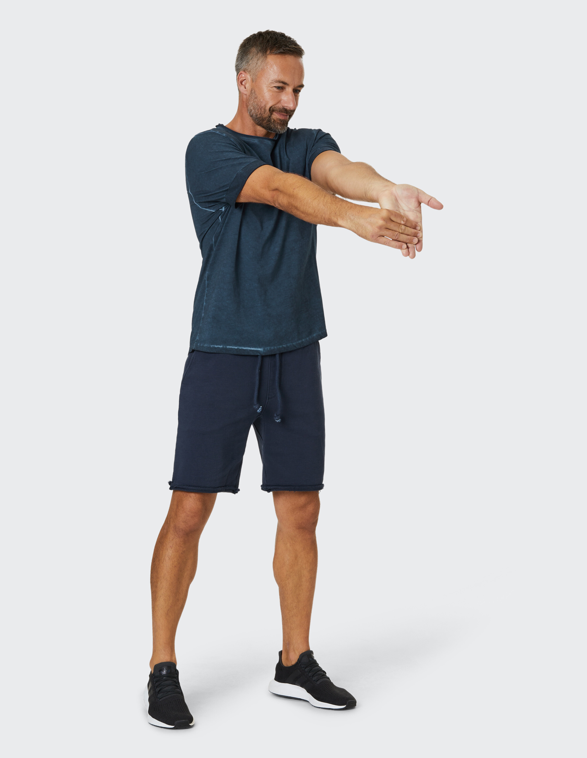 Mann trägt ein blaues T-Shirt und dunkelblaue Shorts und streckt sich in bequemer, lässiger Loungewear.