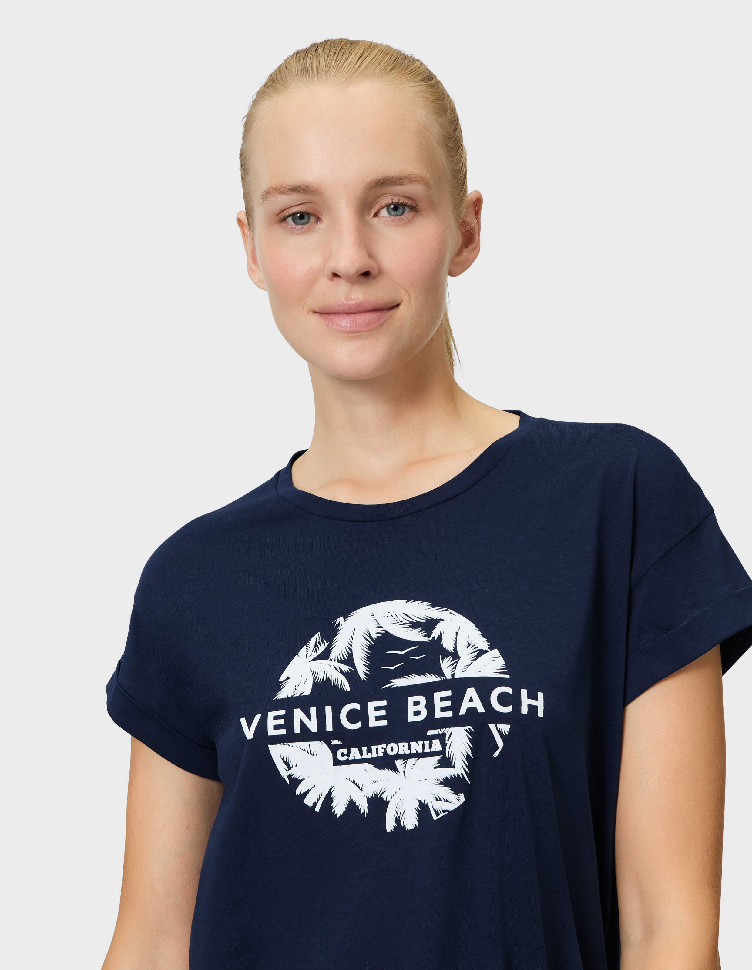 Frau trägt ein marineblaues Freizeit-T-Shirt mit weißem Venice Beach-Grafikdruck.