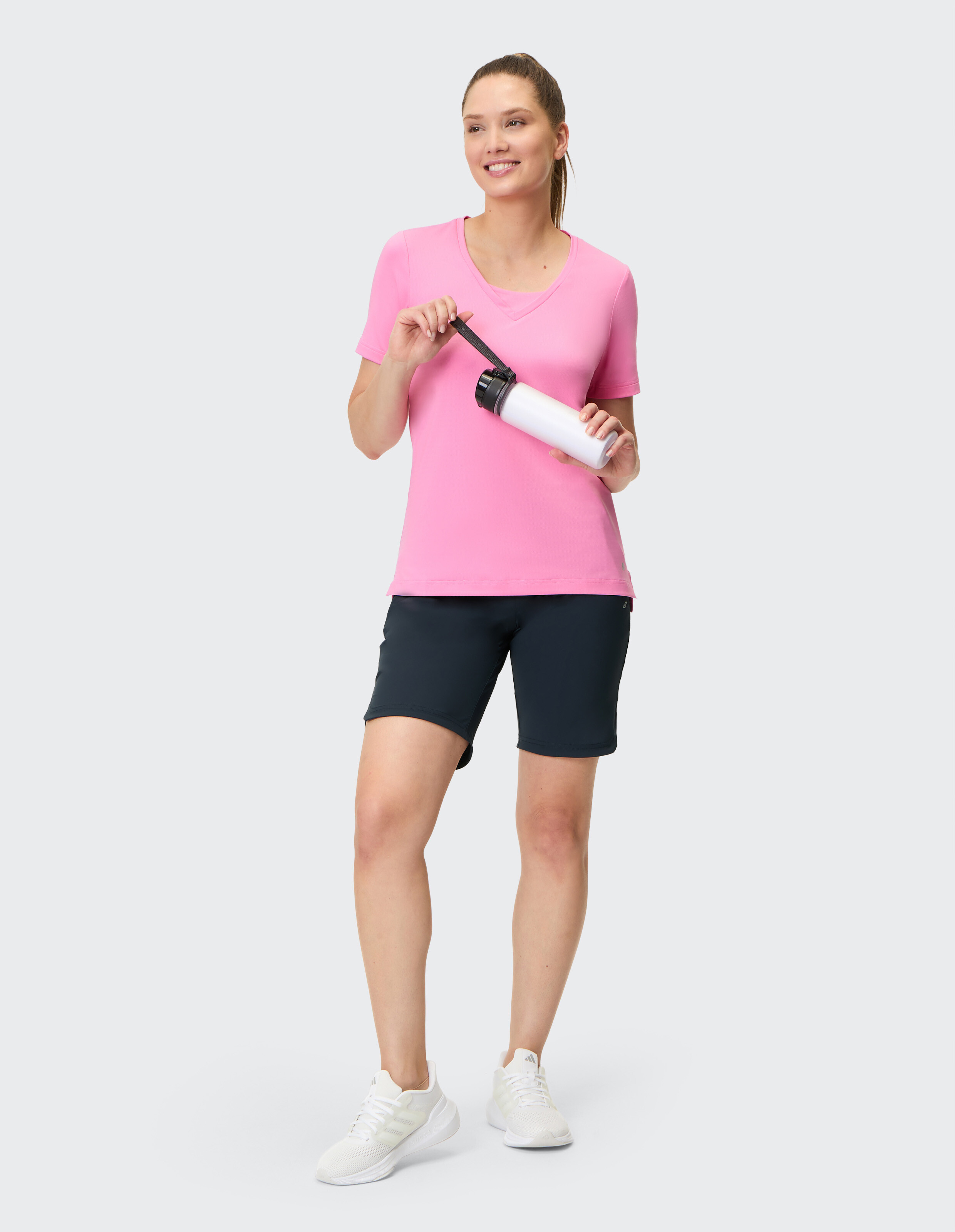 Frau in rosa T-Shirt mit V-Ausschnitt und schwarzen Shorts hält eine Wasserflasche in der Hand.