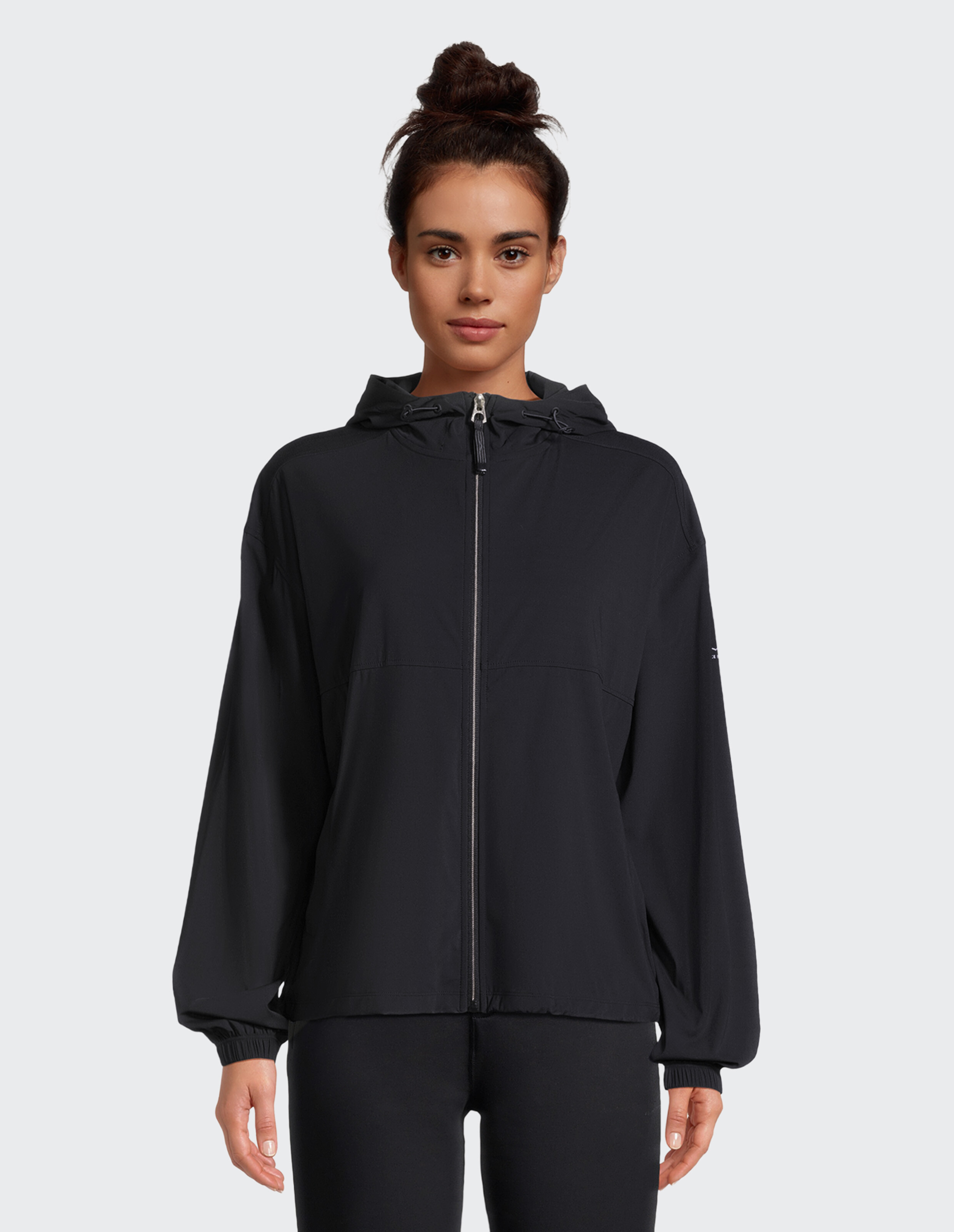 Frau trägt eine schwarze, lässige Kapuzenjacke mit Reißverschluss für bequeme Reise- und Loungewear.