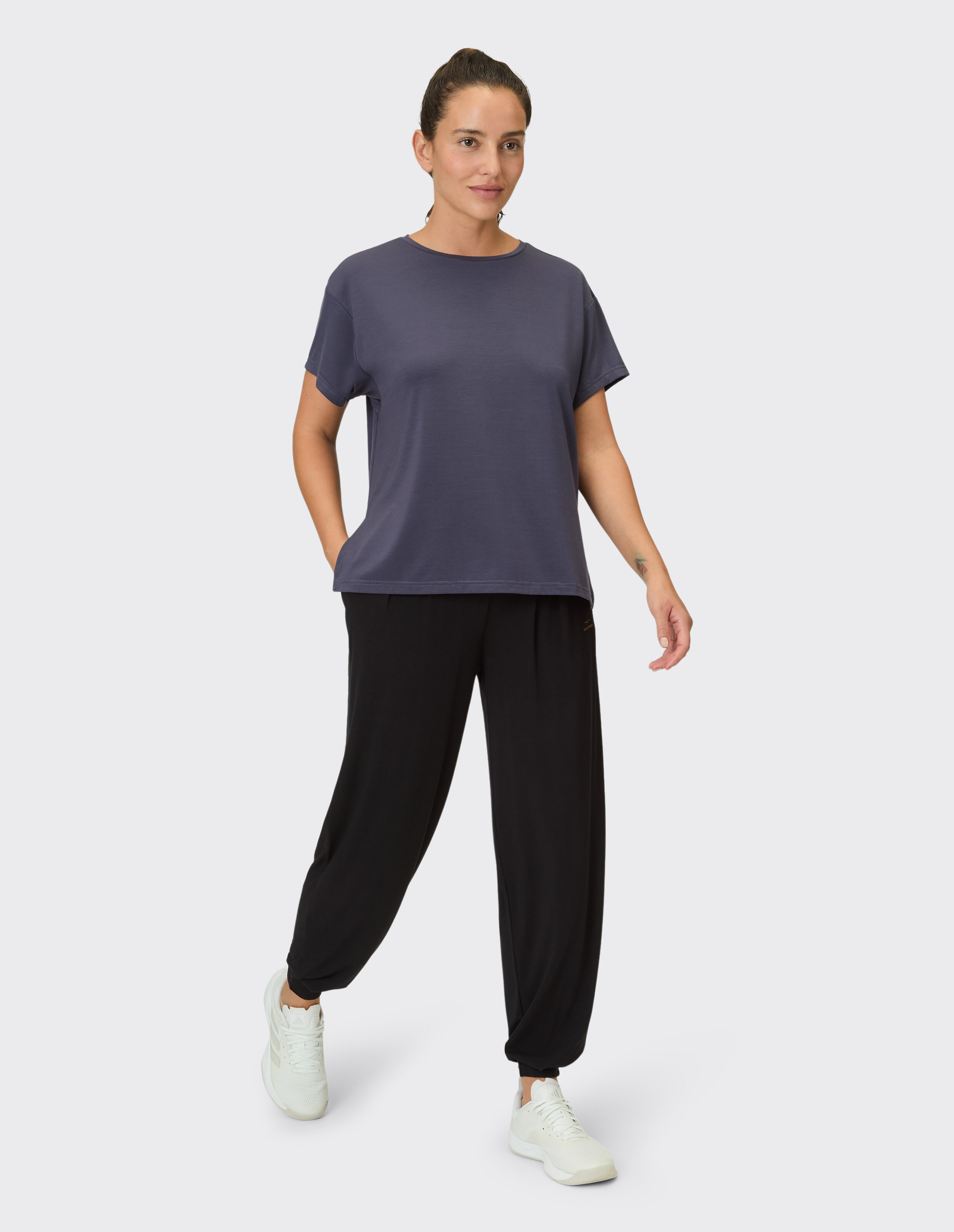 Frau trägt ein graues Salma-Kurzarmhemd von Venice Beach und schwarze lässige Jogginghosen.