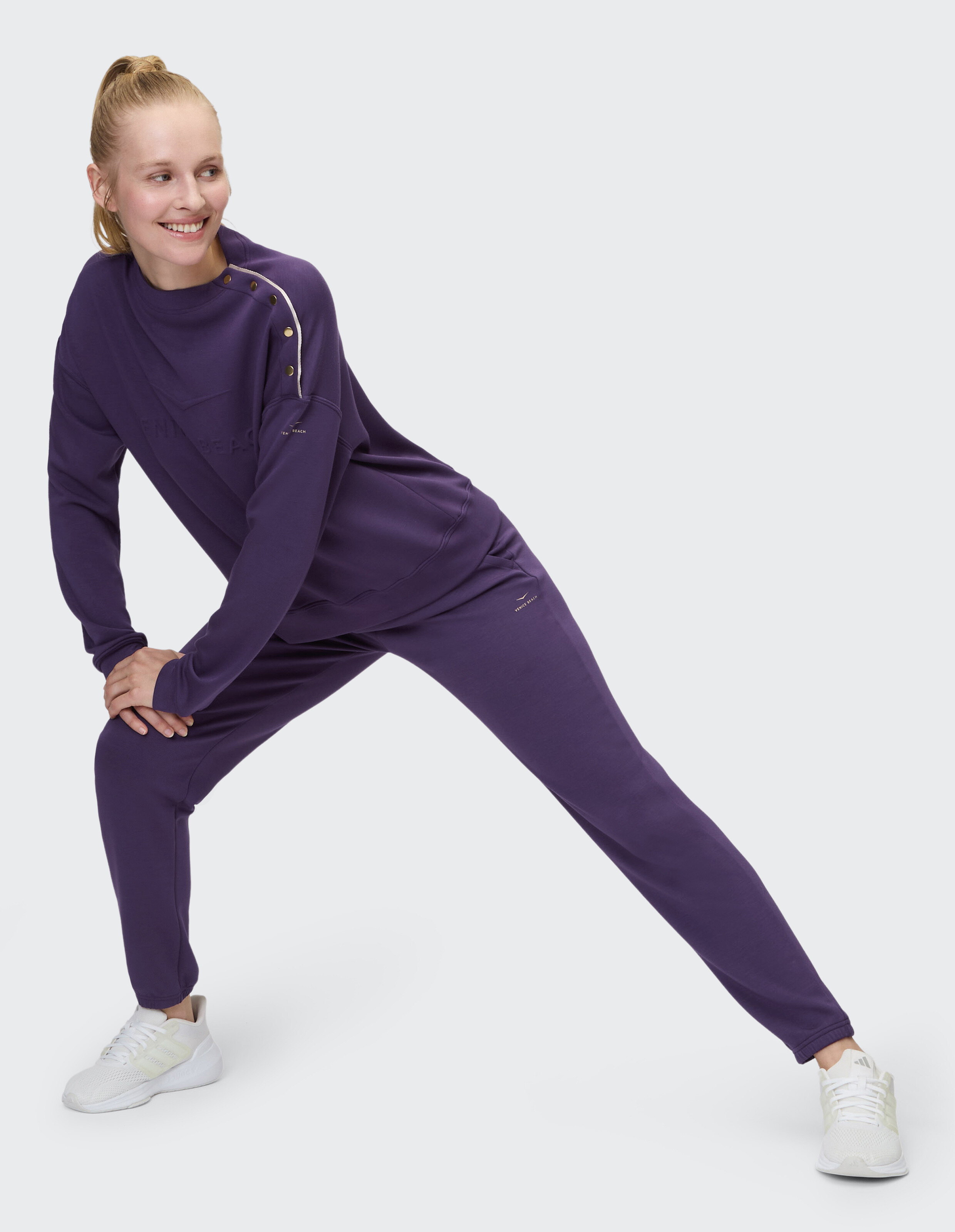 Model in einem lila Freizeit-Trainingsanzug, der eine entspannte Passform und ein stilvolles Design zur Schau stellt.