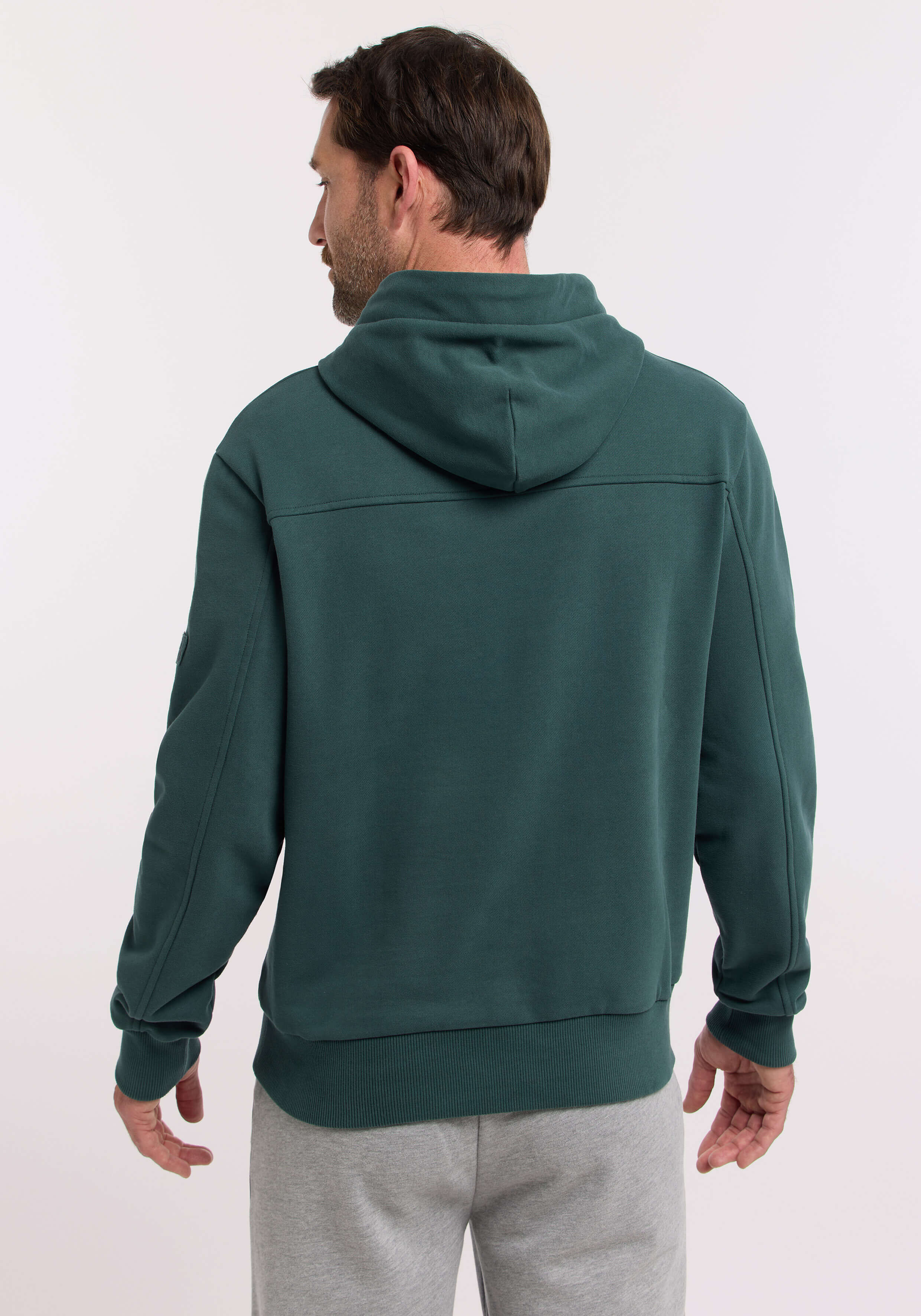 Mann trägt einen kuscheligen dunkelgrünen Kapuzenpullover zum lässigen Faulenzen, Rückansicht.
