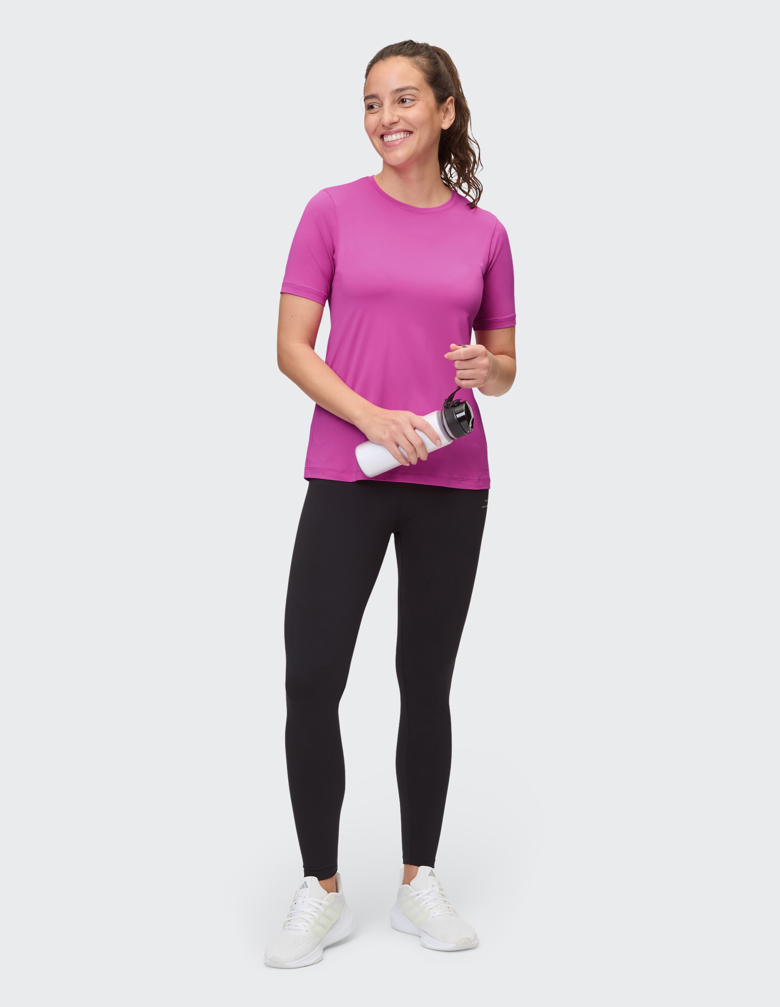 Frau trägt ein rosa T-Shirt und schwarze Leggings und hält eine Wasserflasche in der Hand.