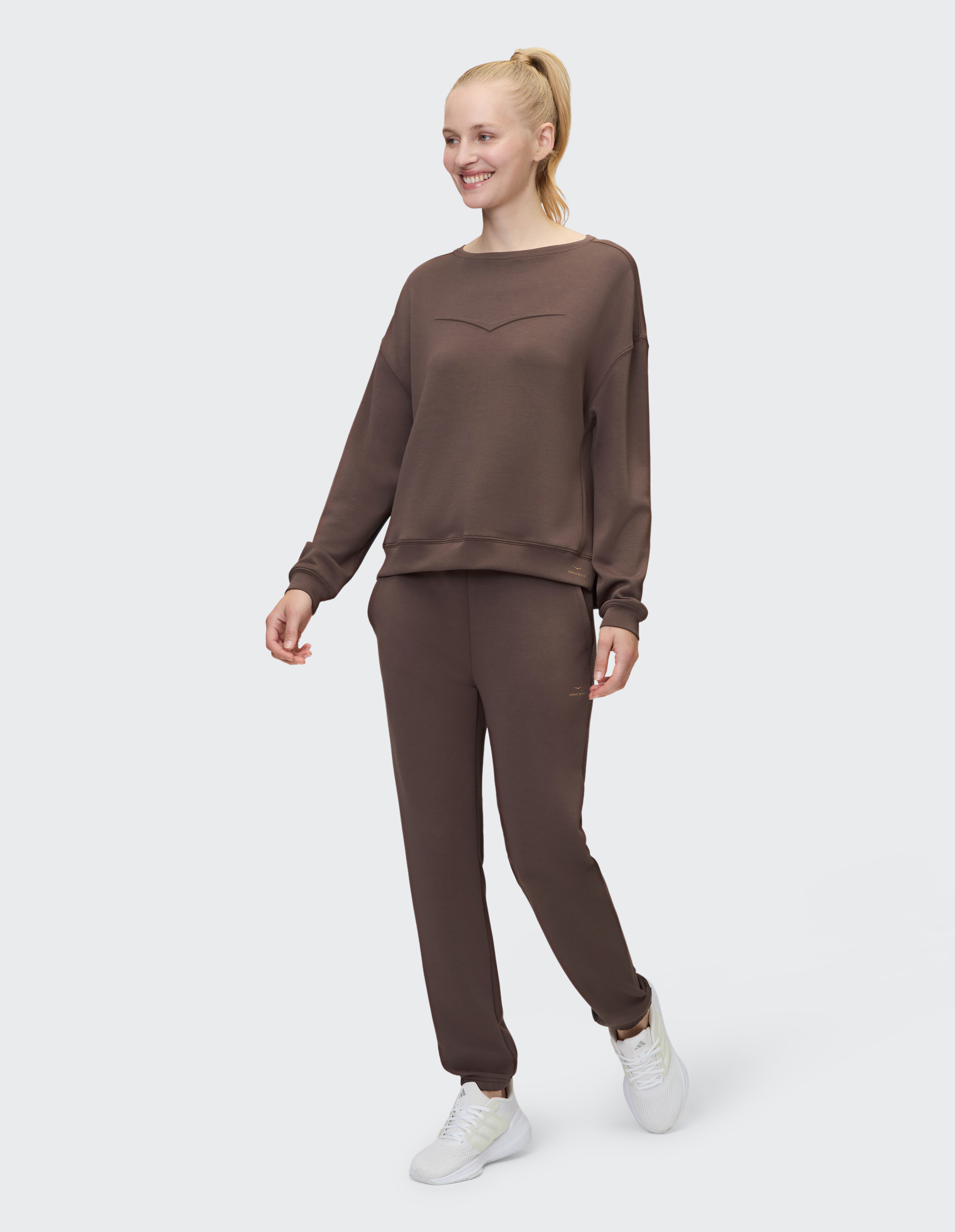 Frau trägt ein gemütliches braunes Lounge-Set mit Sweatshirt und passender Jogginghose.