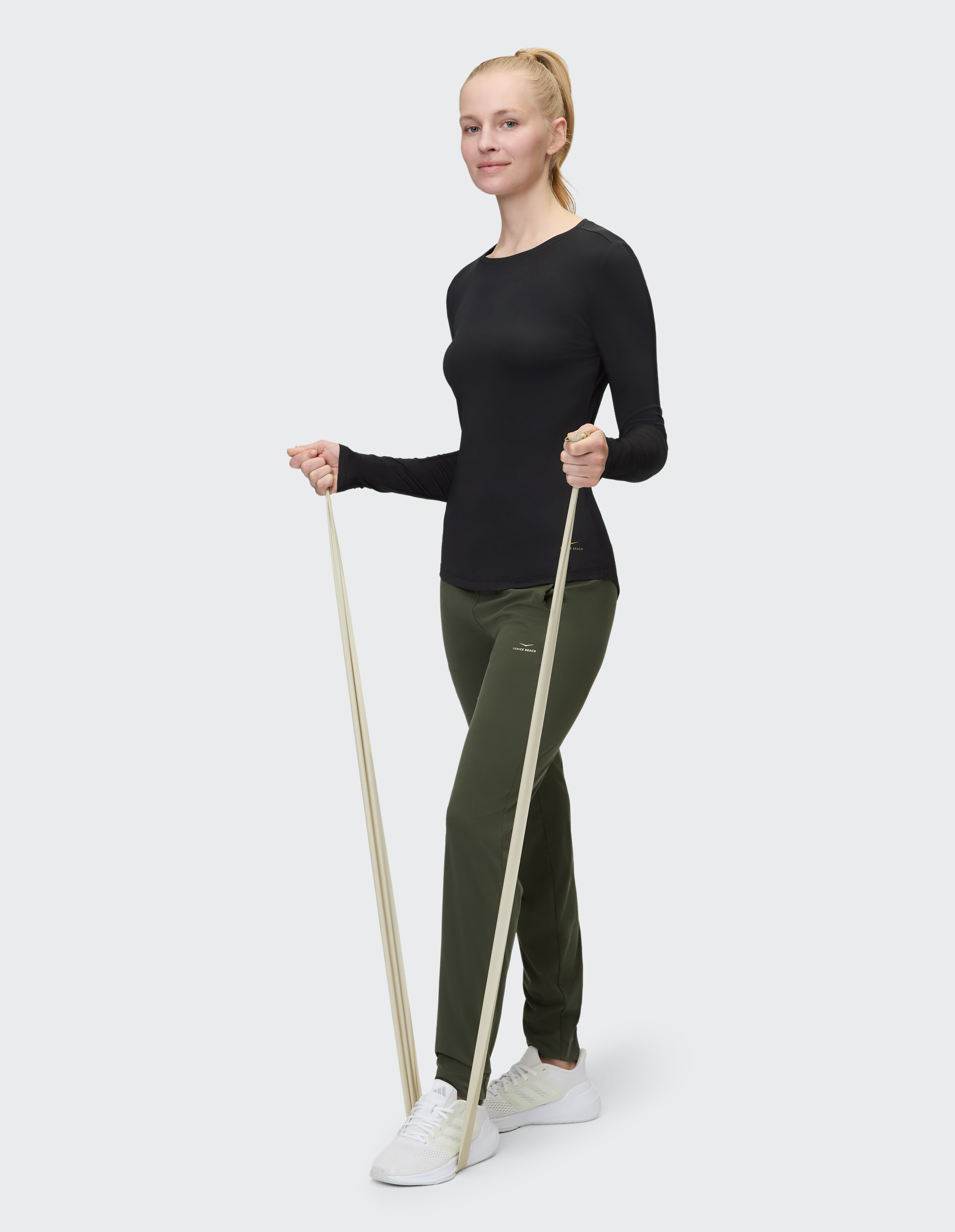 Frau in schwarzem Langarmshirt und olivfarbener Jogginghose trainiert mit einem Widerstandsband.