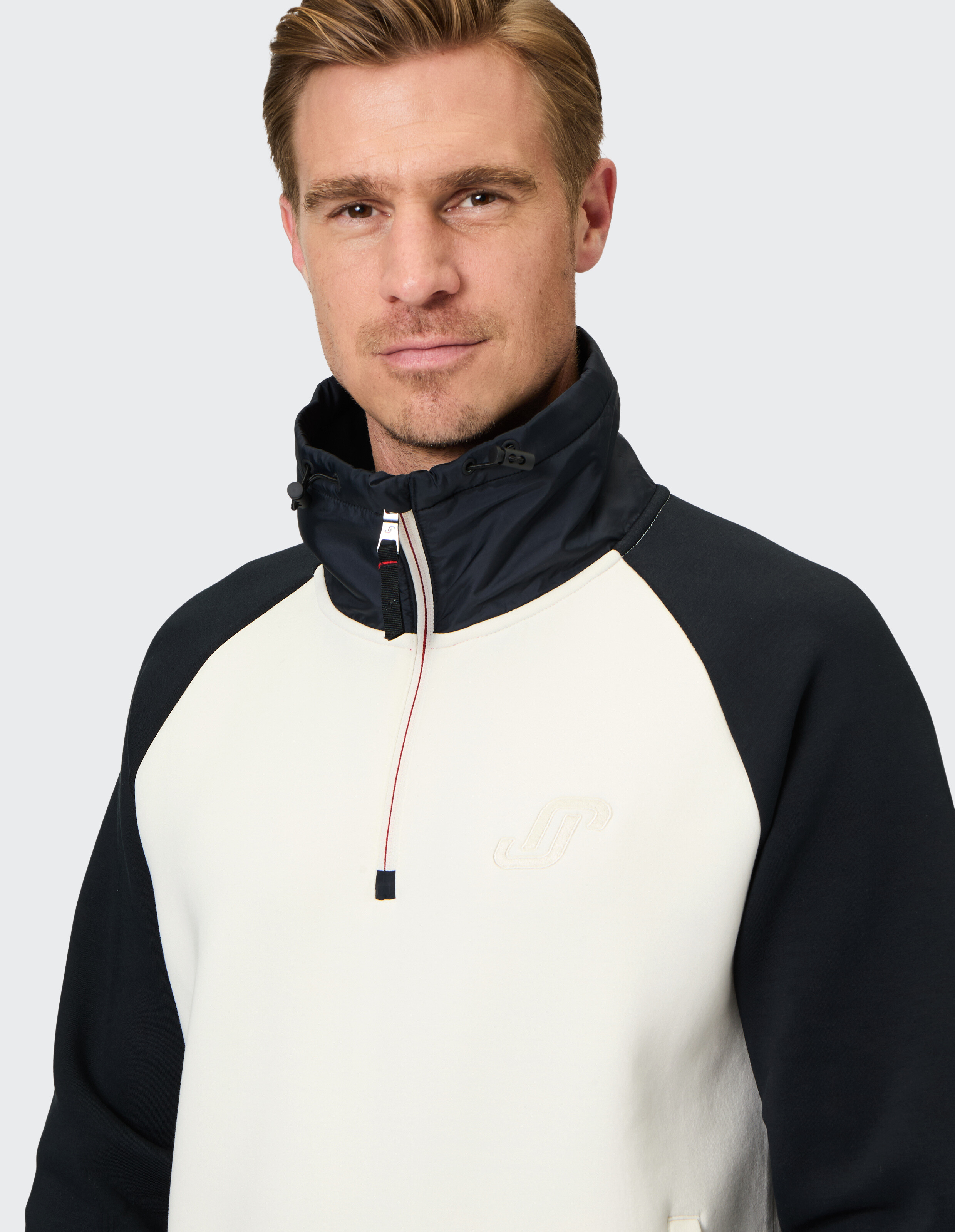 Mann trägt ein cremefarbenes und schwarzes ELBSAND-Sweatshirt mit Viertelreißverschluss und hohem Kragen.