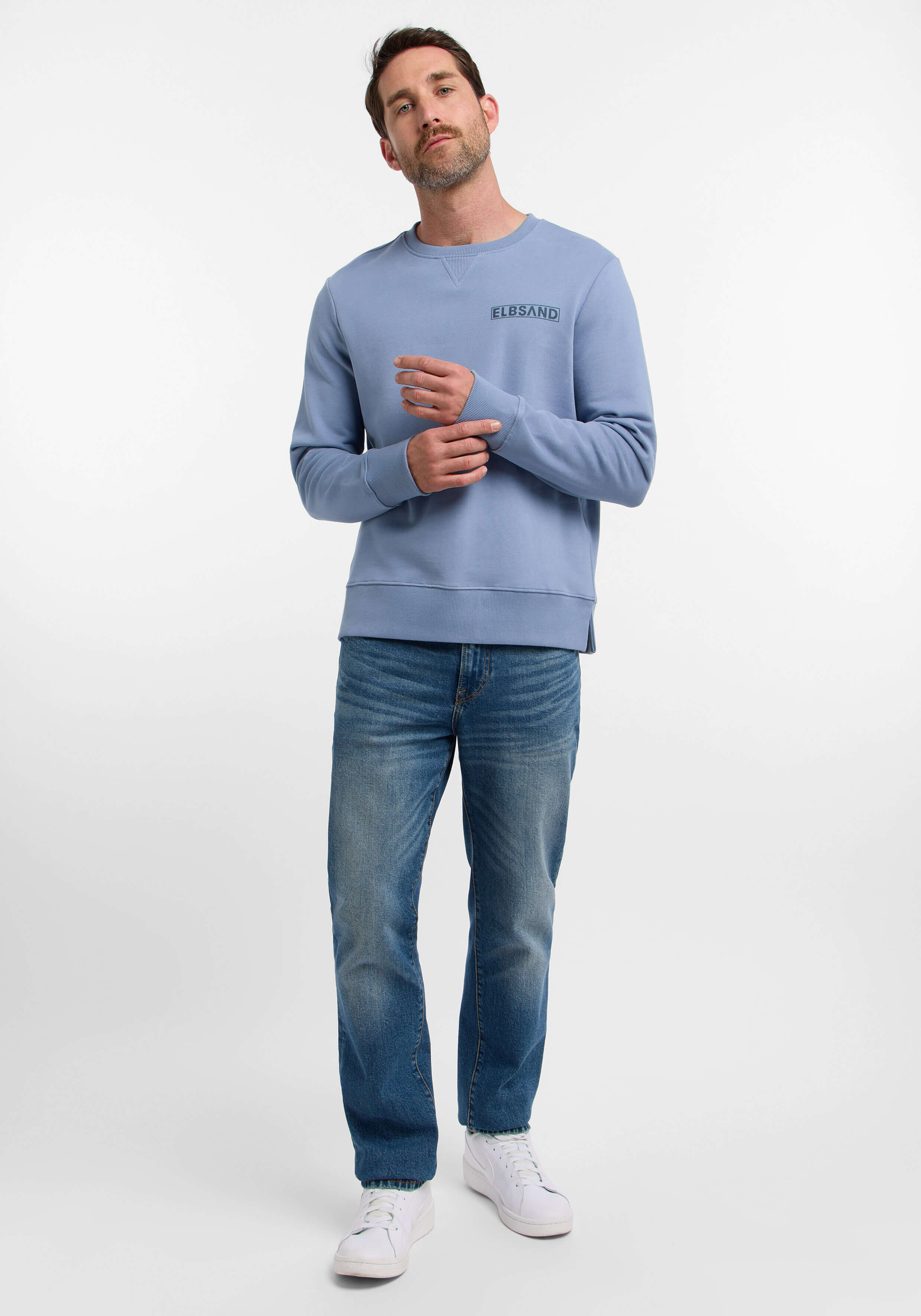 Mann trägt ein hellblaues ELBSAND-Sweatshirt und blaue Jeans für einen lässigen Look.