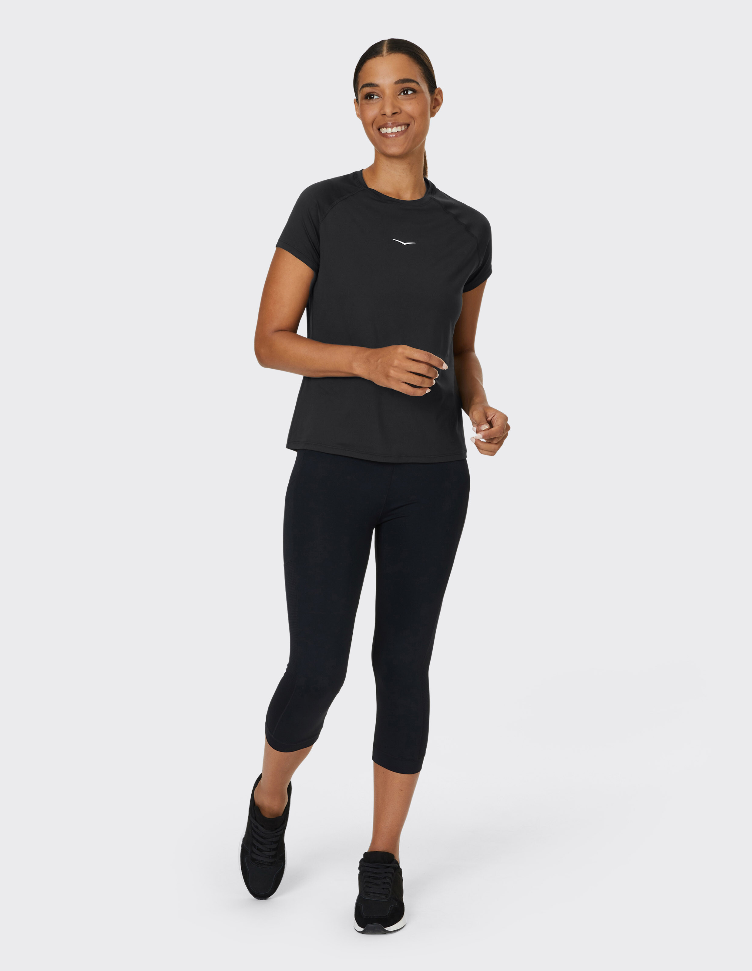Frau in schwarzem Sporttop und Leggings lächelt und geht lässig.