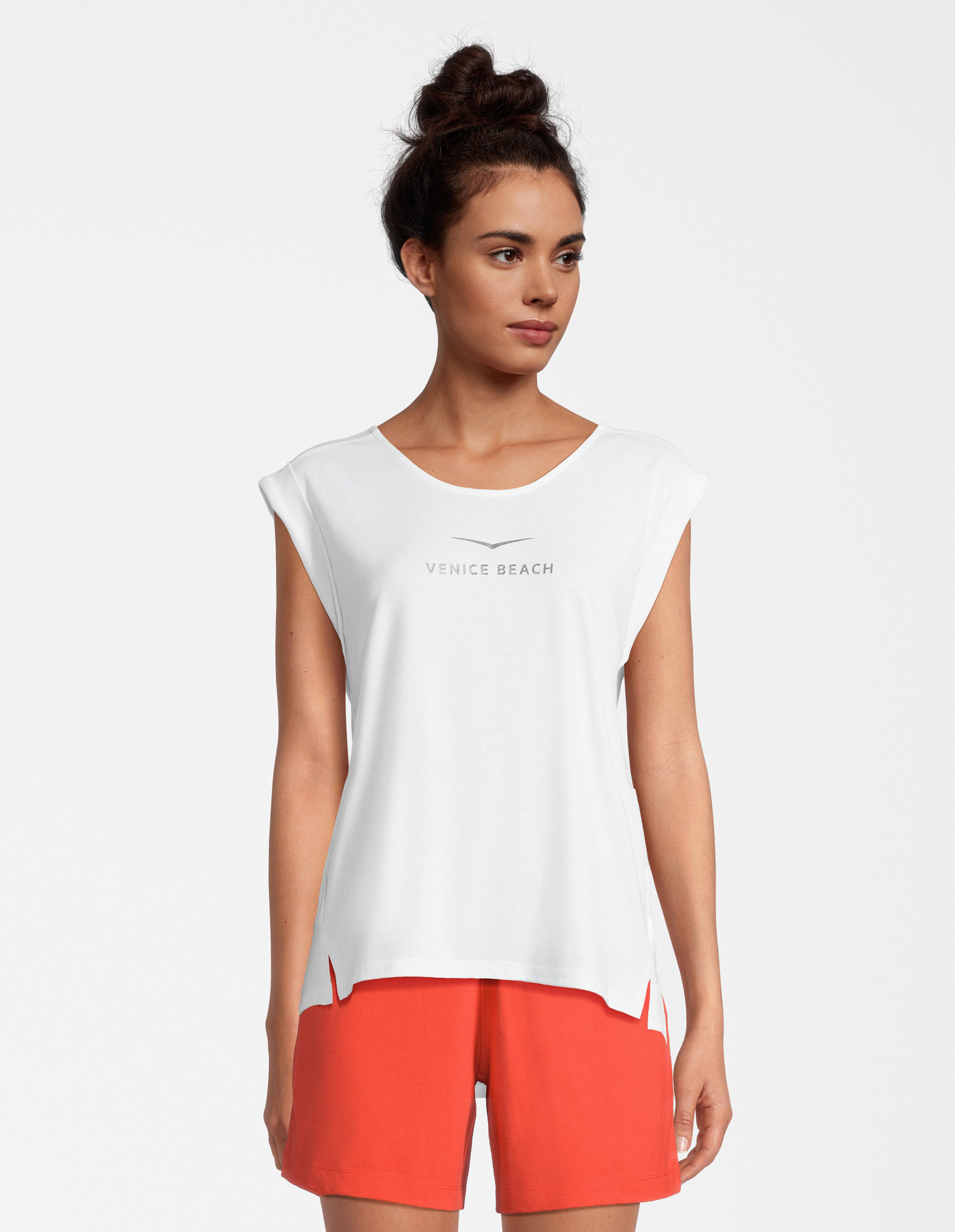 Frau trägt ein weißes lässiges Venice Beach-T-Shirt mit orangefarbenen Shorts zum Entspannen.