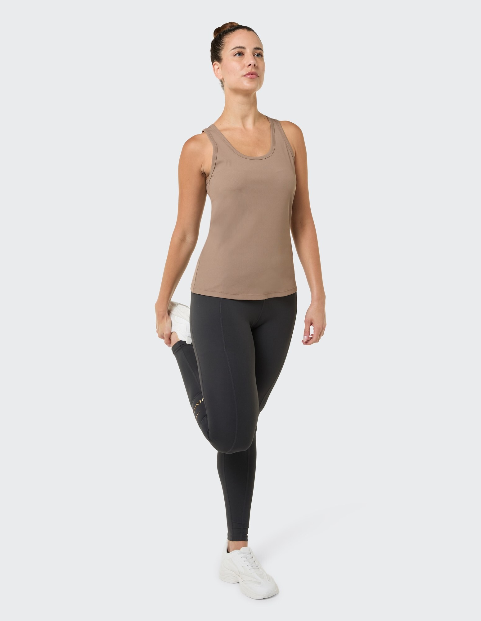 Frau in braunem Tanktop und schwarzen Leggings, die sich in lässiger Sportkleidung dehnt.