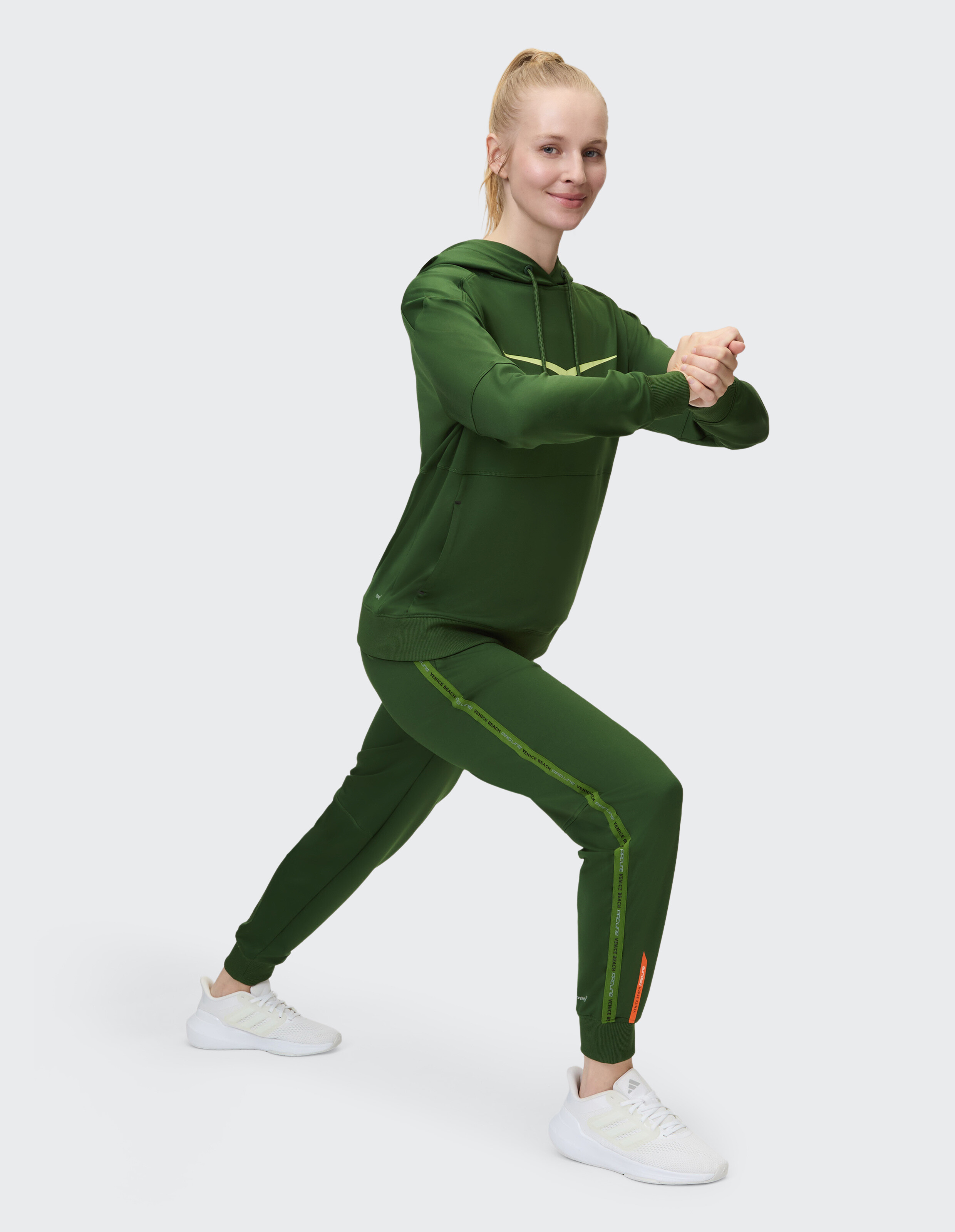 Frau in einem grünen Kapuzenpullover und passenden Joggern macht einen Ausfallschritt zum Training.