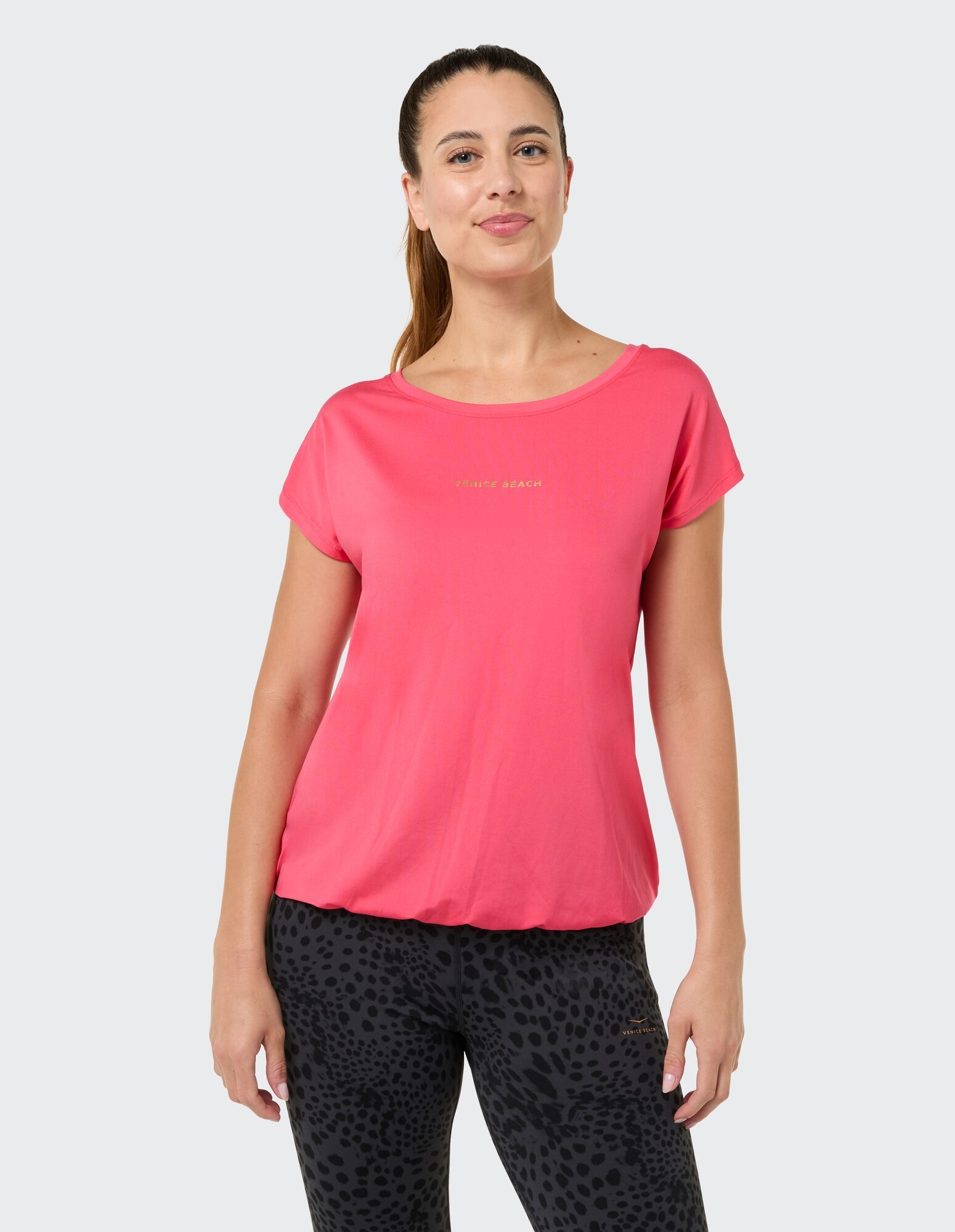 Frau in einem rosa Freizeitoberteil mit goldenem Schriftzug und schwarz gemusterten Leggings.