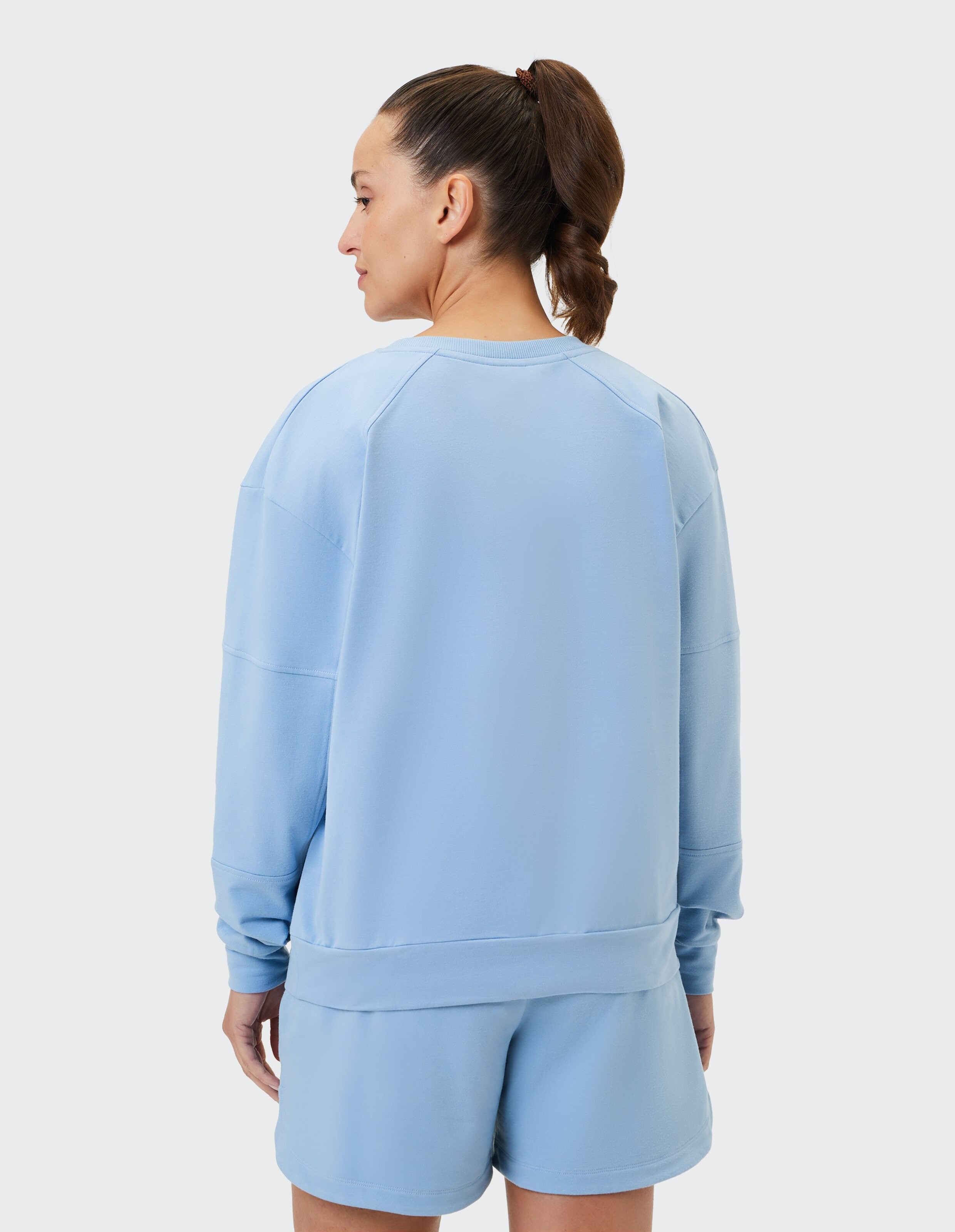 Frau in einem hellblauen, lässigen Sweatshirt und Shorts, die eine entspannte Passform zeigen.