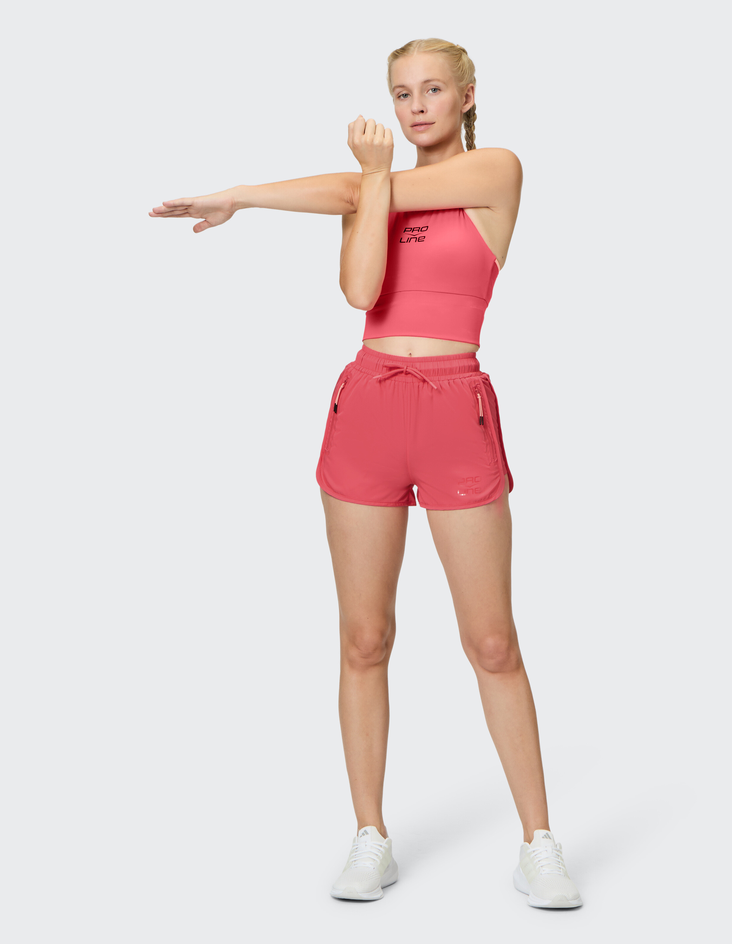 Frau beim Stretching in einem rosa Crop-Top und passenden Shorts, ideal für ungezwungene Workouts.