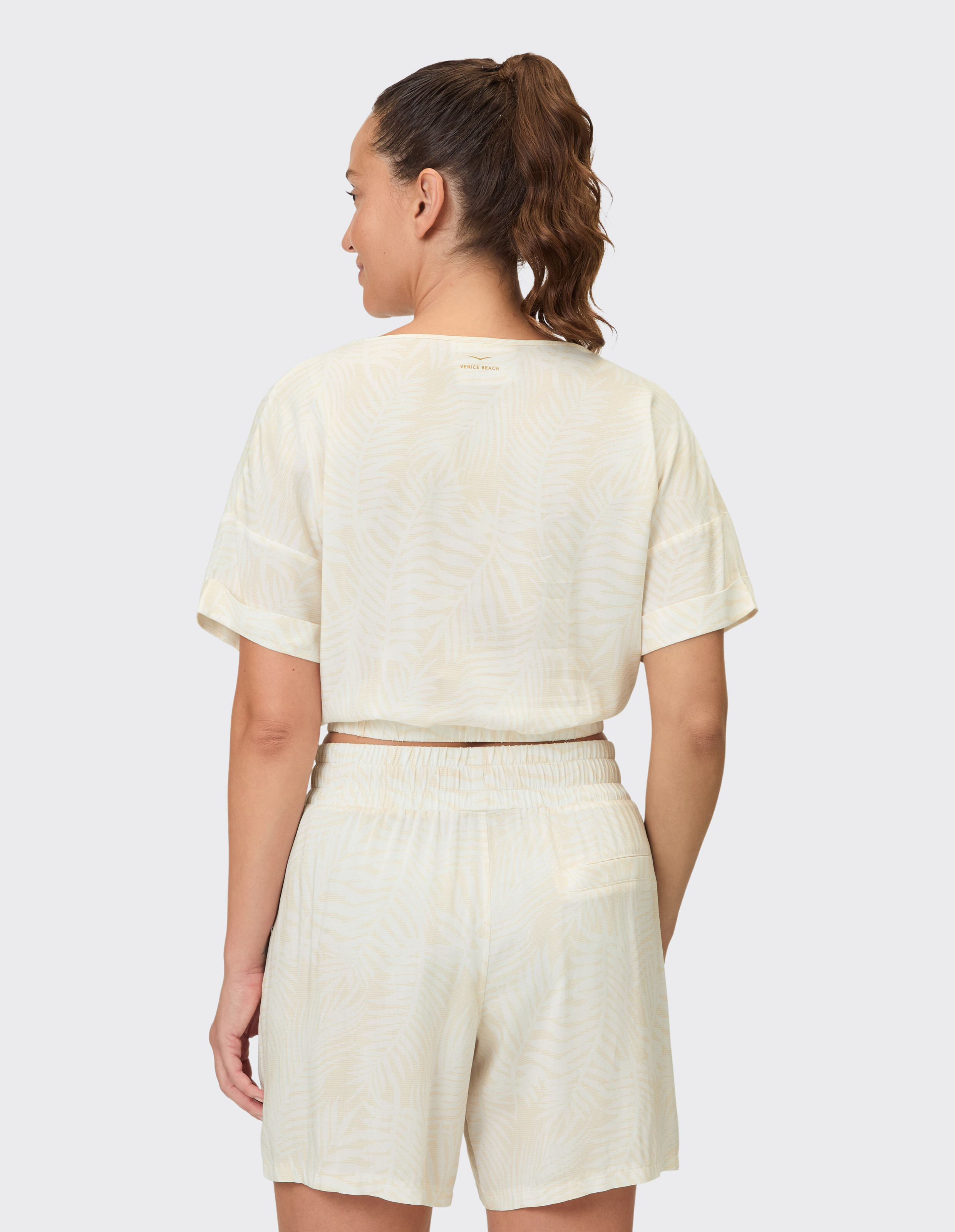 Frau trägt ein beiges Lounge-Set mit Palmenmuster, einem kurzen Oberteil und elastischen Shorts.