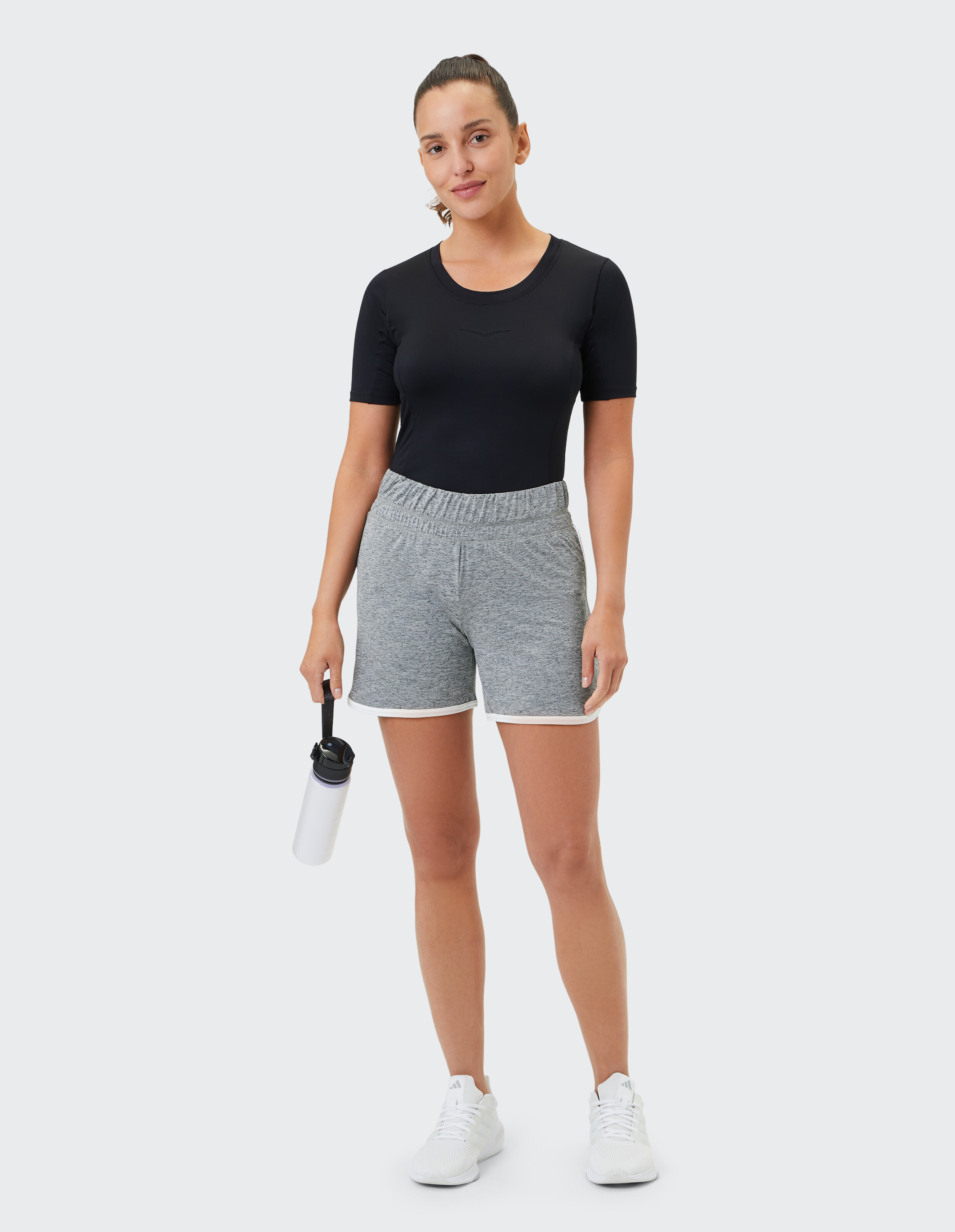 Frau trägt ein schwarzes T-Shirt und graue Freizeitshorts und hält eine Wasserflasche in der Hand.