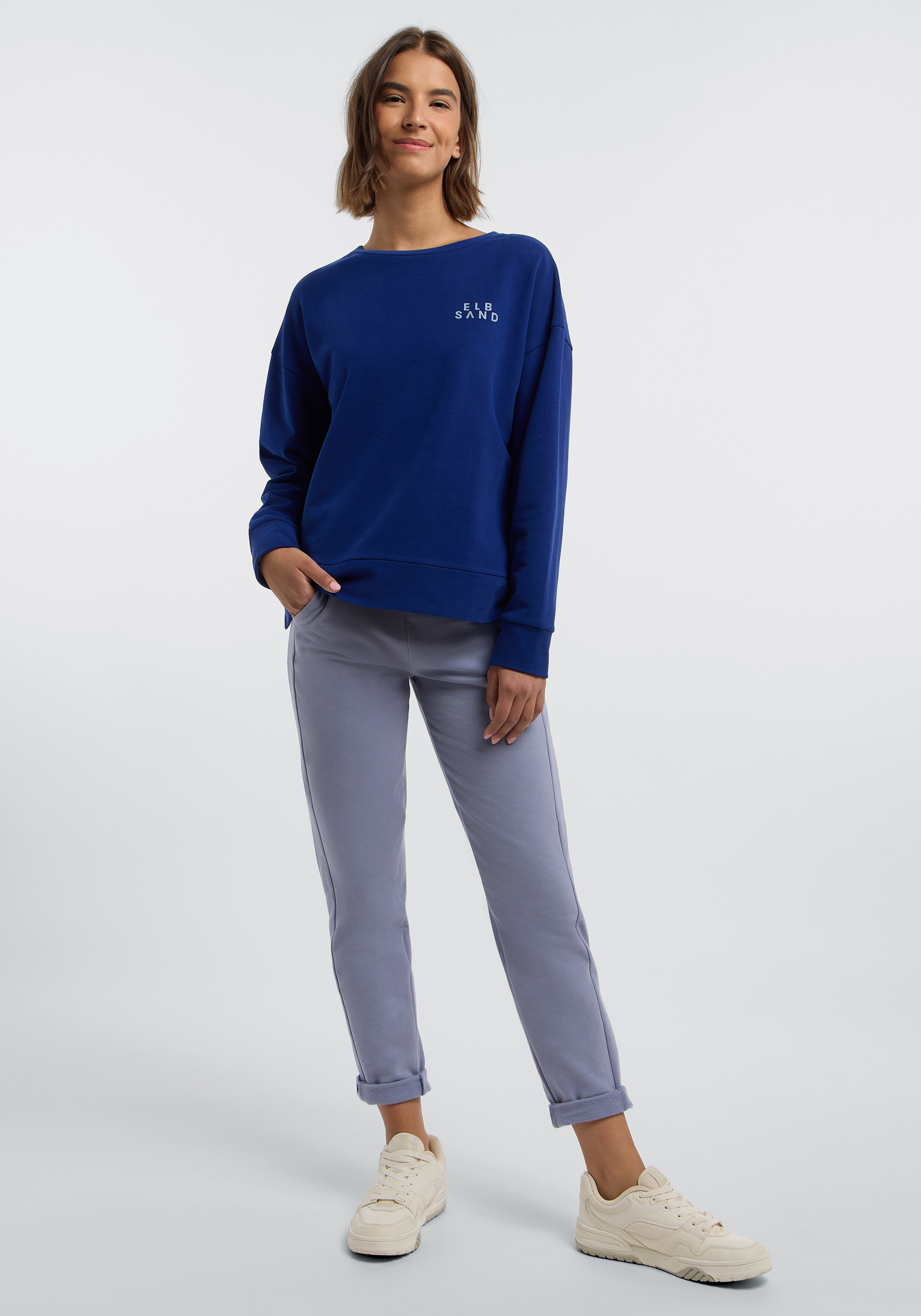 Frau trägt ein blaues ELBSAND-Sweatshirt und eine graue Freizeithose für einen bequemen Look.
