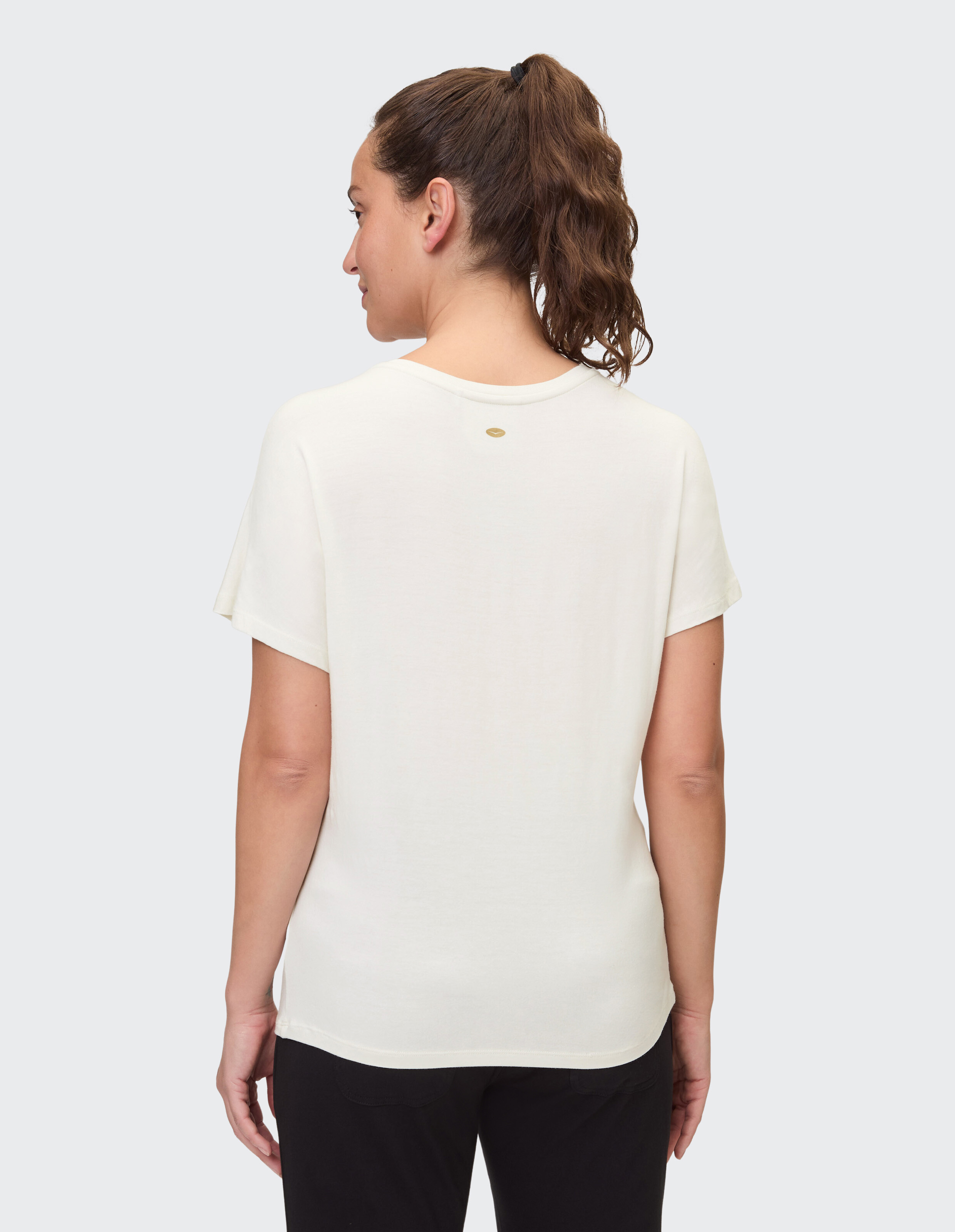 Frau trägt ein gemütliches, lässiges cremefarbenes T-Shirt mit kleinem Logo, Rückansicht.