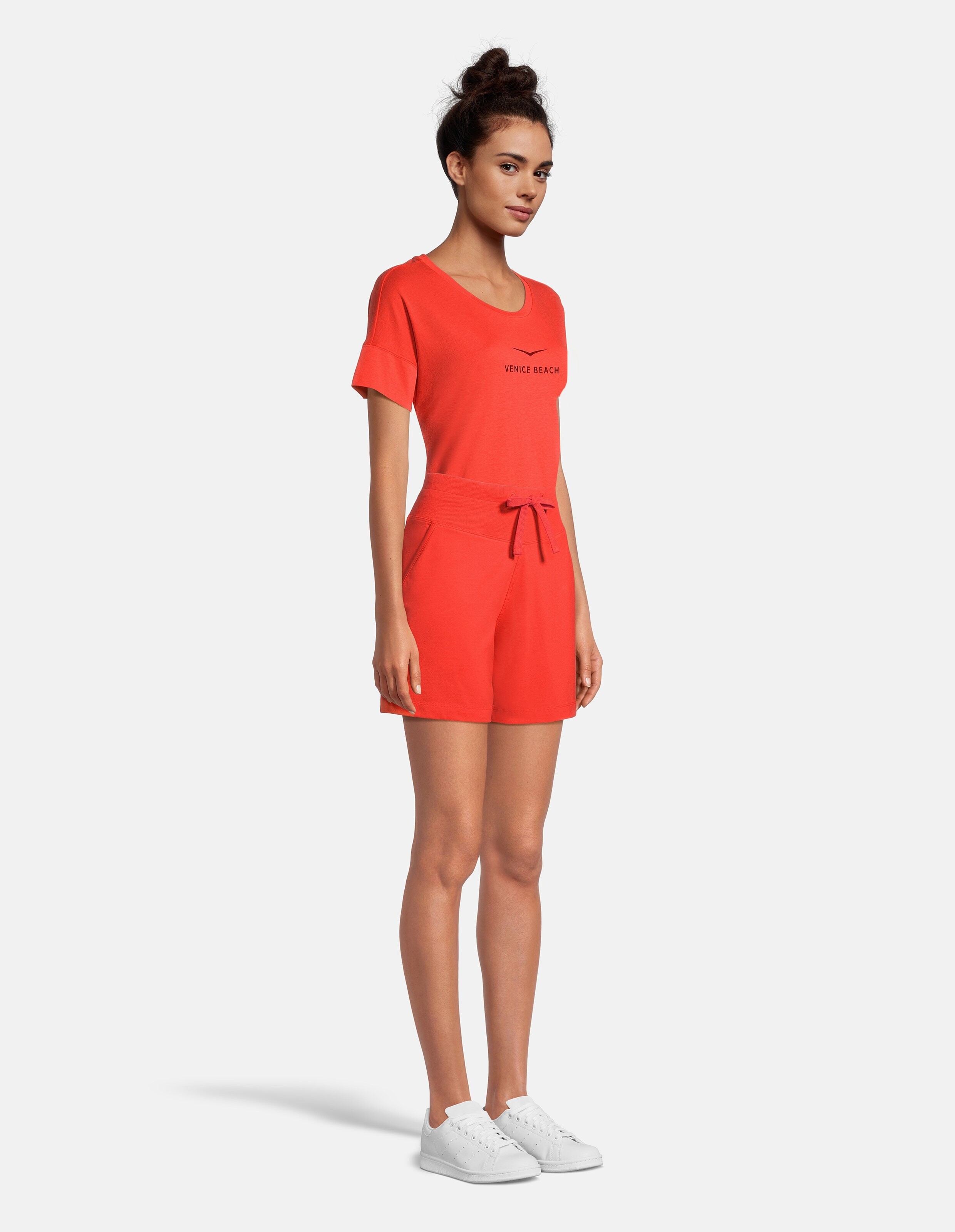 Das Model trägt ein rotes Freizeitoutfit mit einem kurzärmeligen Oberteil und Shorts.