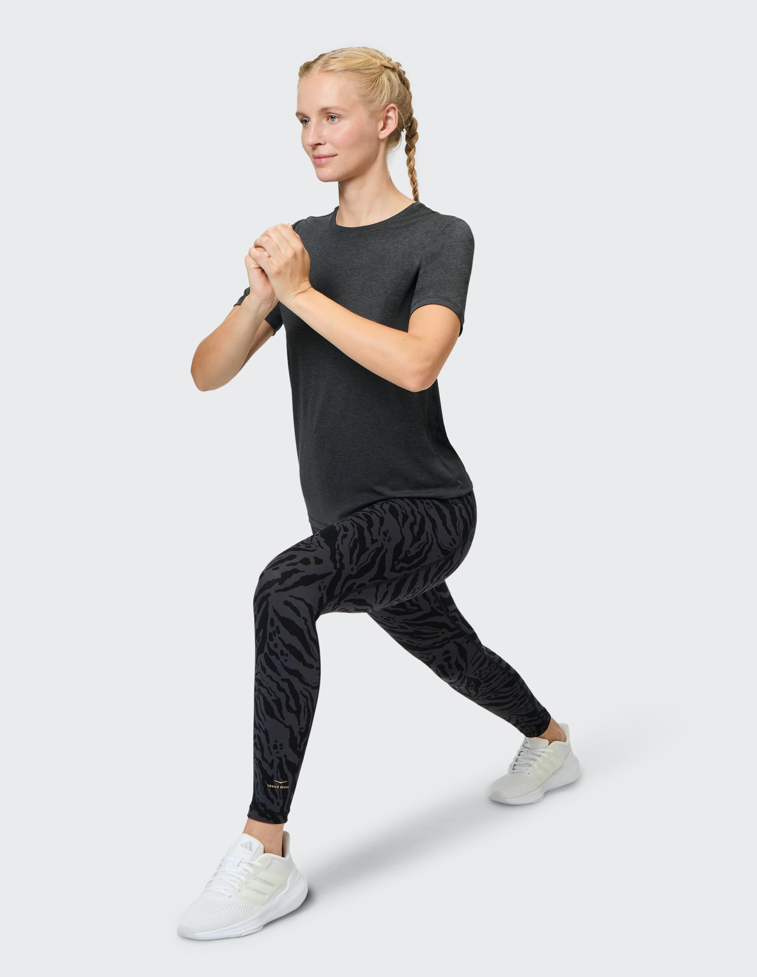 Frau in schwarzem T-Shirt und Leggings mit Tigermuster demonstriert eine Ausfallschrittübung.