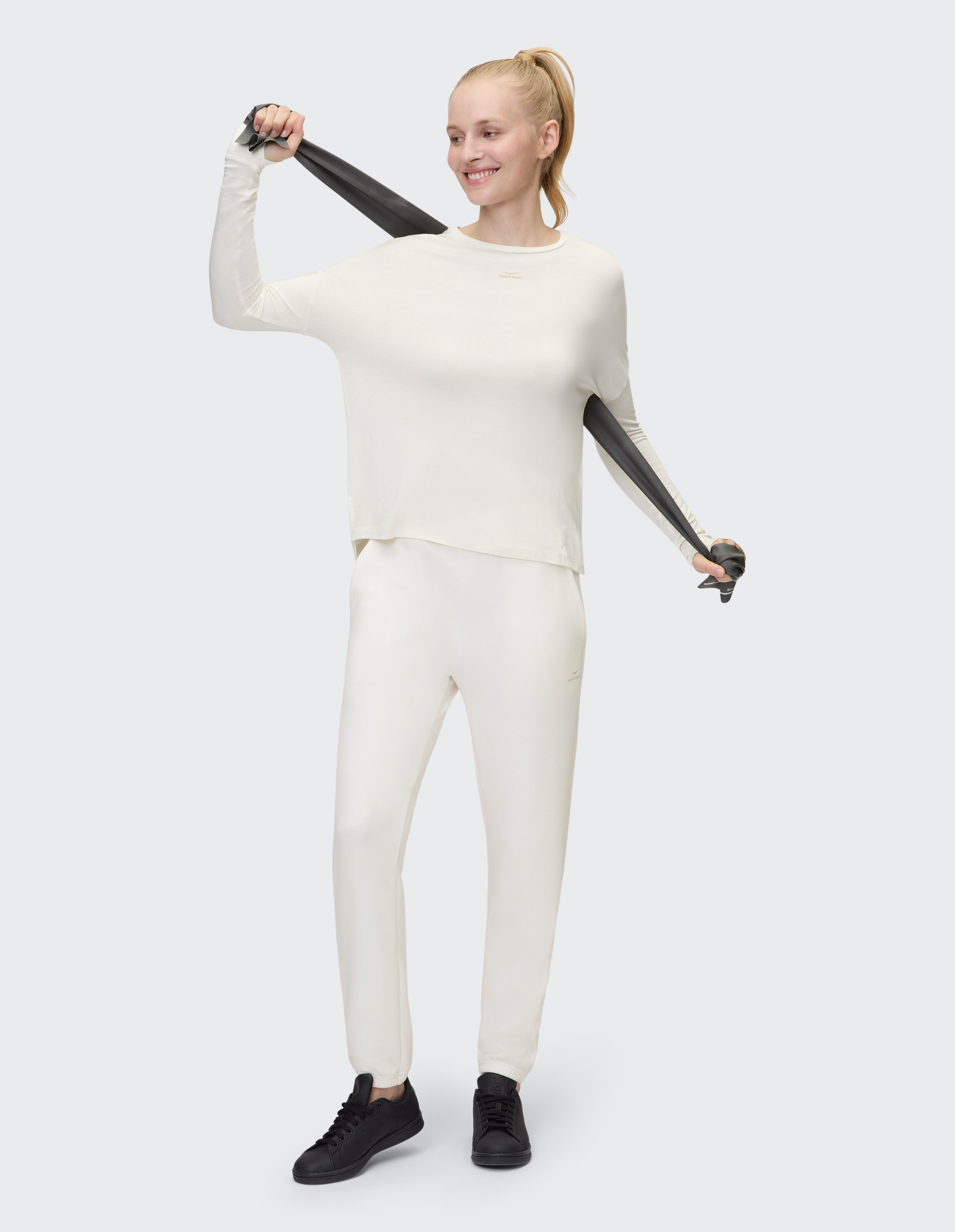 Frau in einem gemütlichen cremefarbenen Loungewear-Set trainiert mit einem schwarzen Widerstandsband.