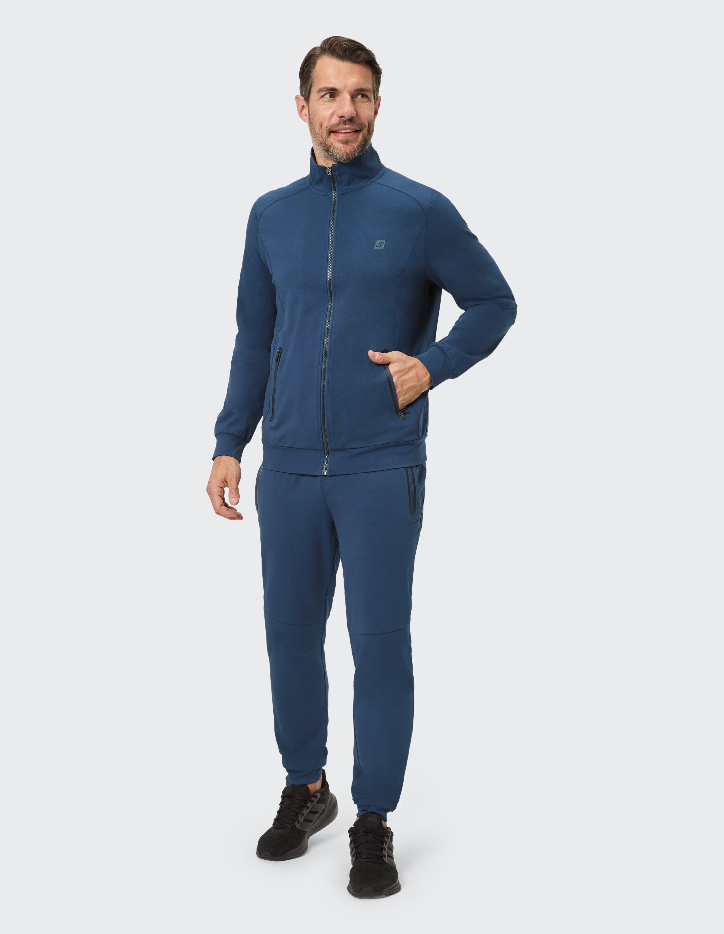 Mann in einer dunkelblauen Jacke mit Reißverschluss und passenden Jogginghosen, stilvolle Freizeitkleidung.
