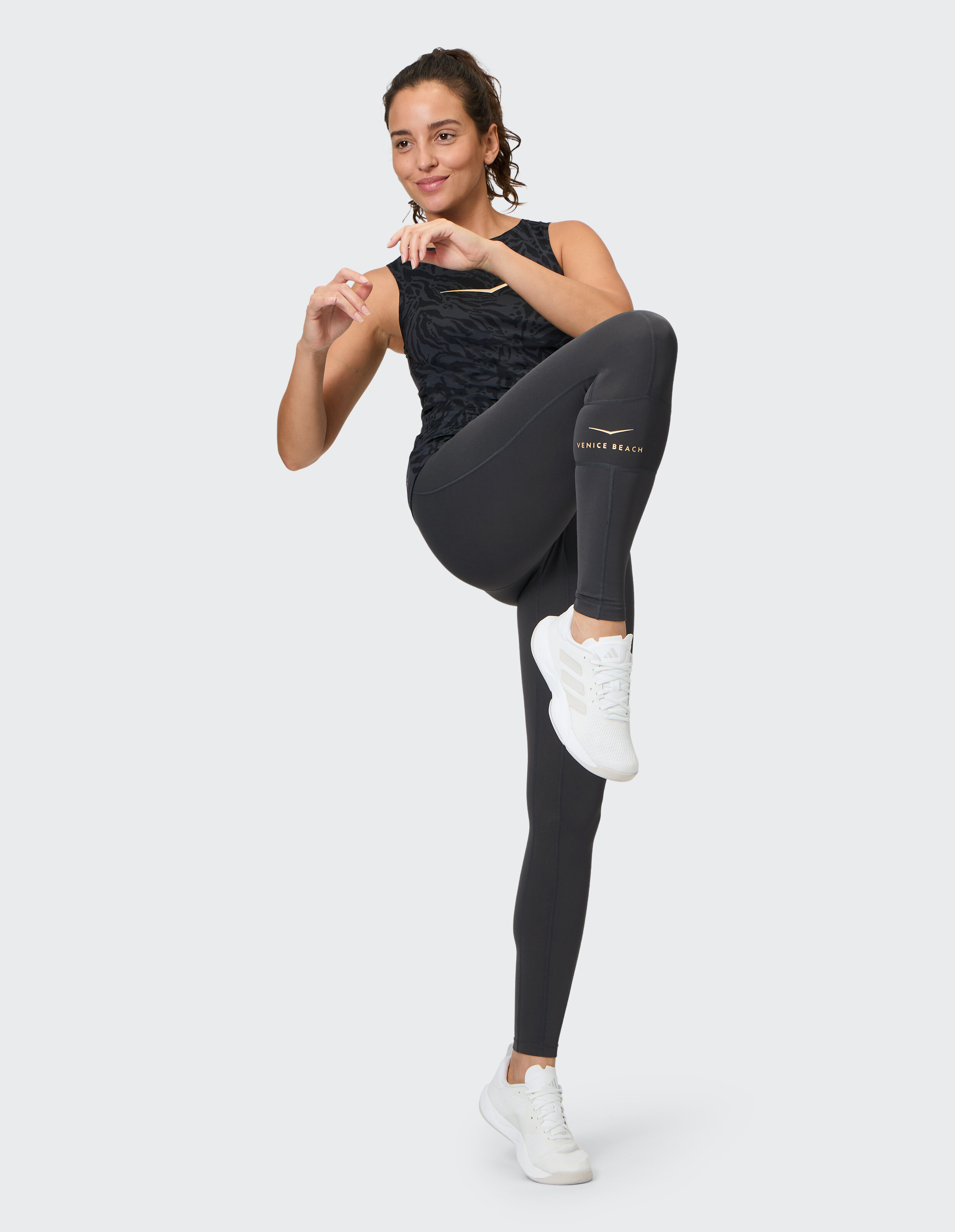 Frau in schwarzen Activewear-Leggings und Tanktop posiert in stylischen Sportschuhen.