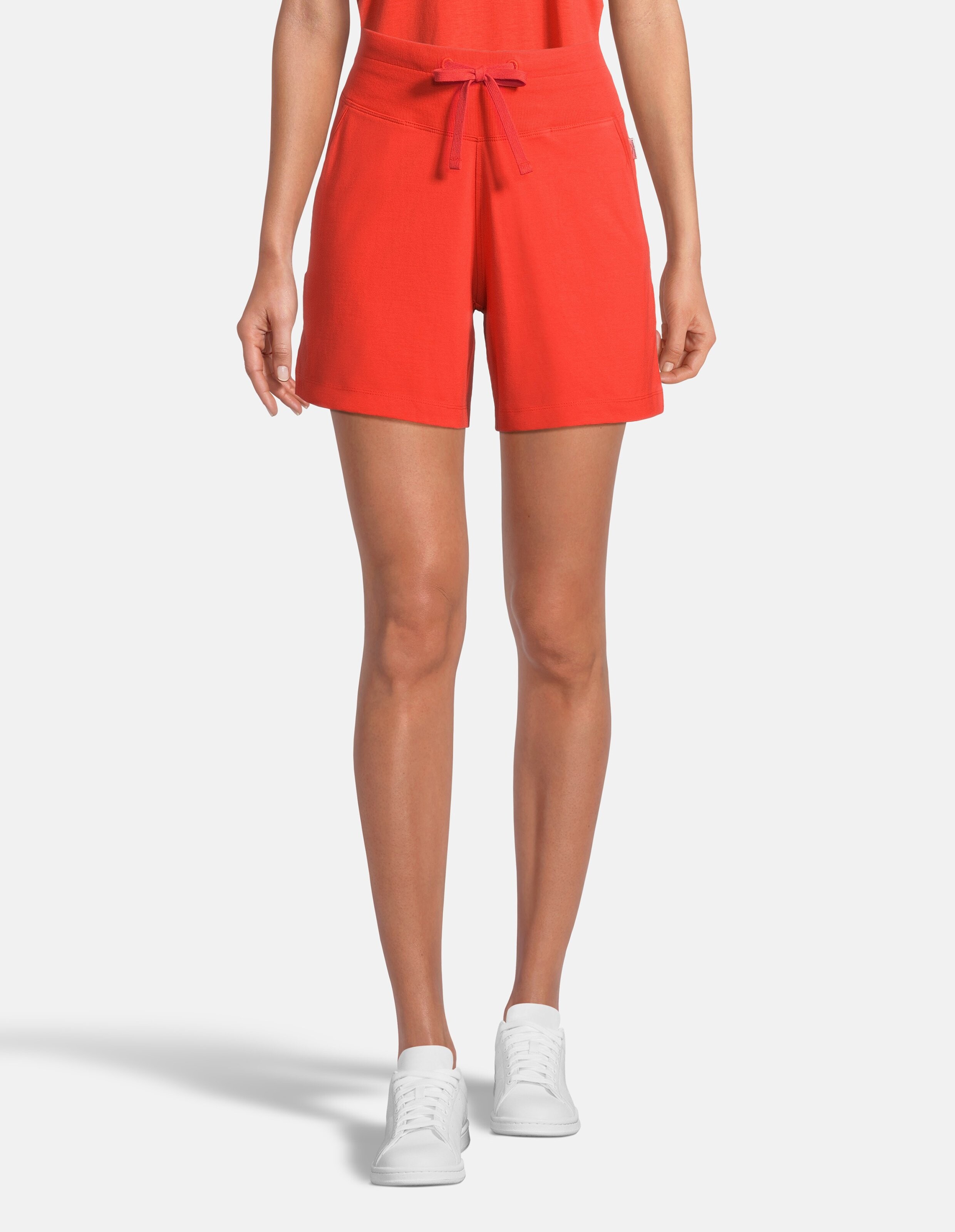 Frau trägt bequeme rote Freizeitshorts mit Kordelzug in der Taille und weiße Turnschuhe.