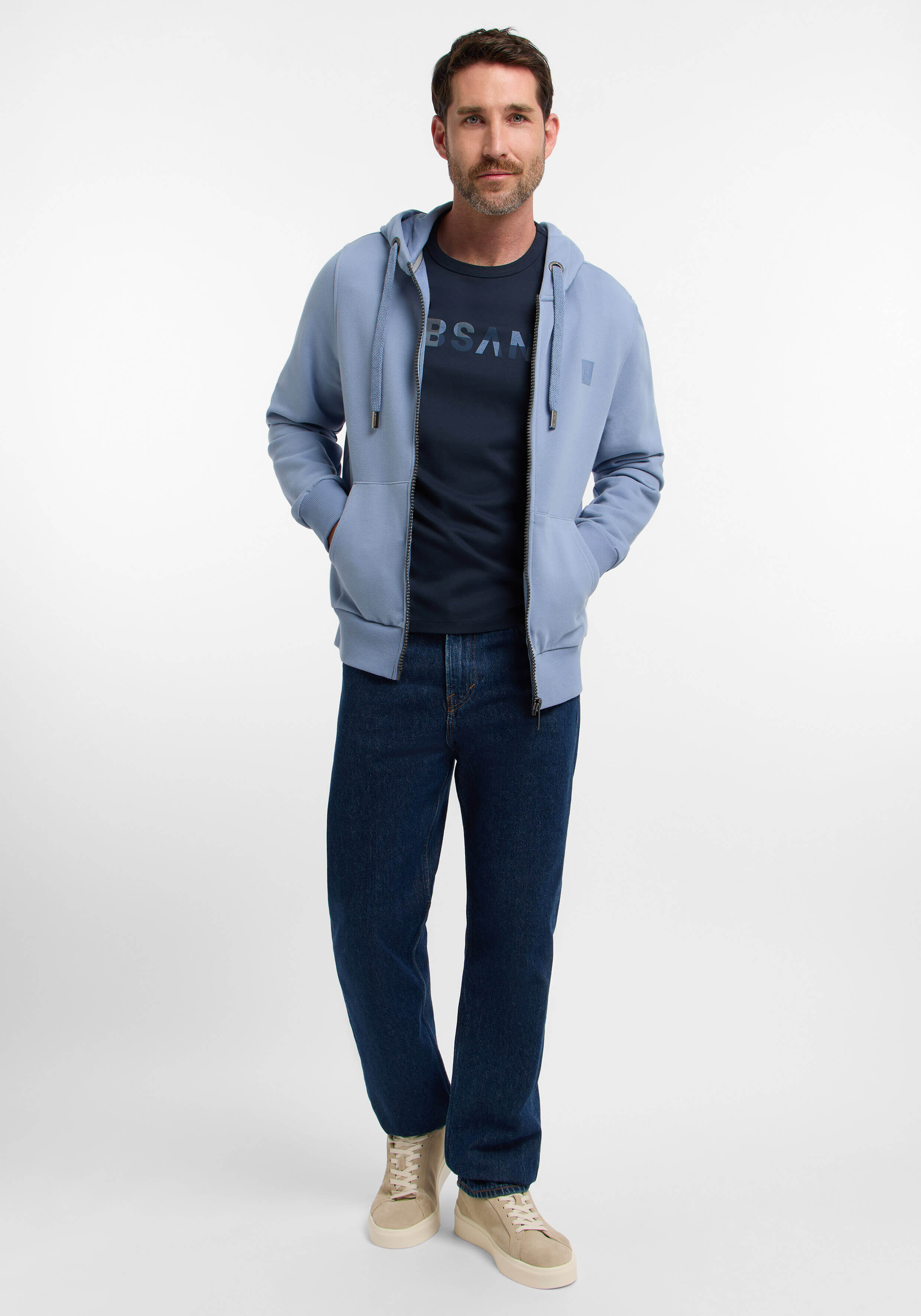 Mann trägt einen hellblauen Kapuzenpullover mit Reißverschluss, ein dunkelblaues T-Shirt und Jeans für einen lässigen Look.