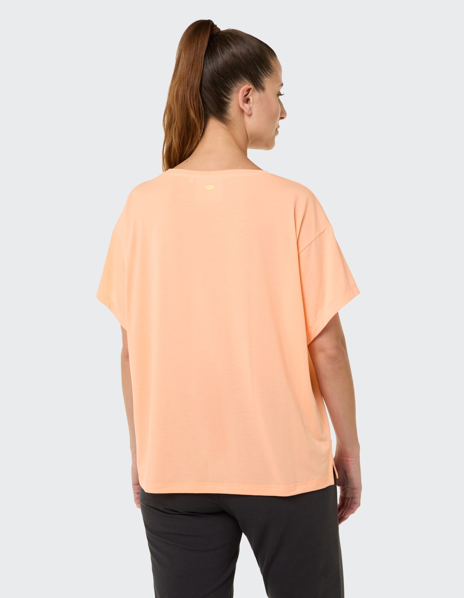 Rückansicht einer Frau, die ein pfirsichfarbenes, übergroßes T-Shirt trägt, perfekt für Freizeitkleidung.