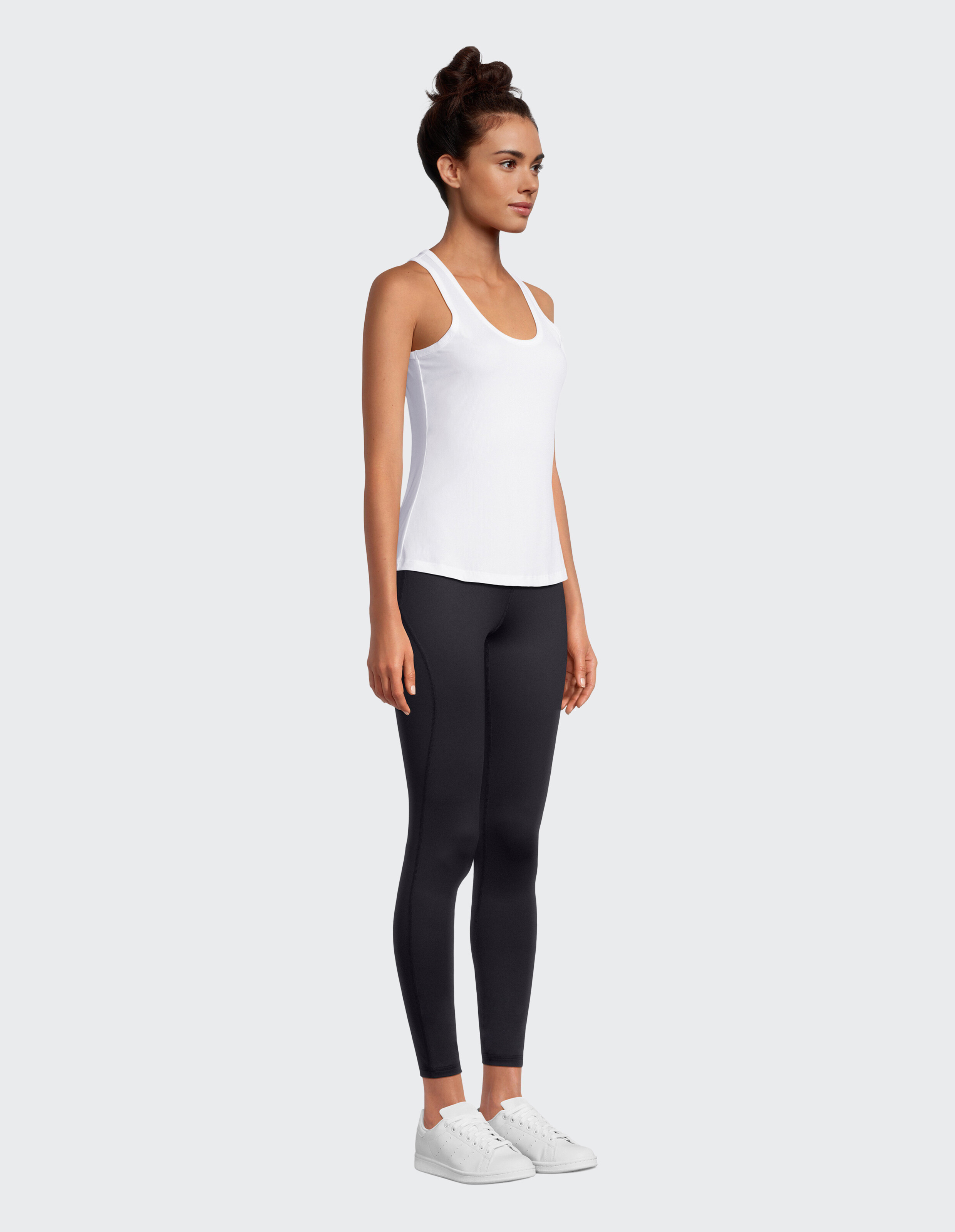 Das Model trägt ein weißes Tanktop und schwarze Leggings, lässig gestylt mit weißen Turnschuhen.