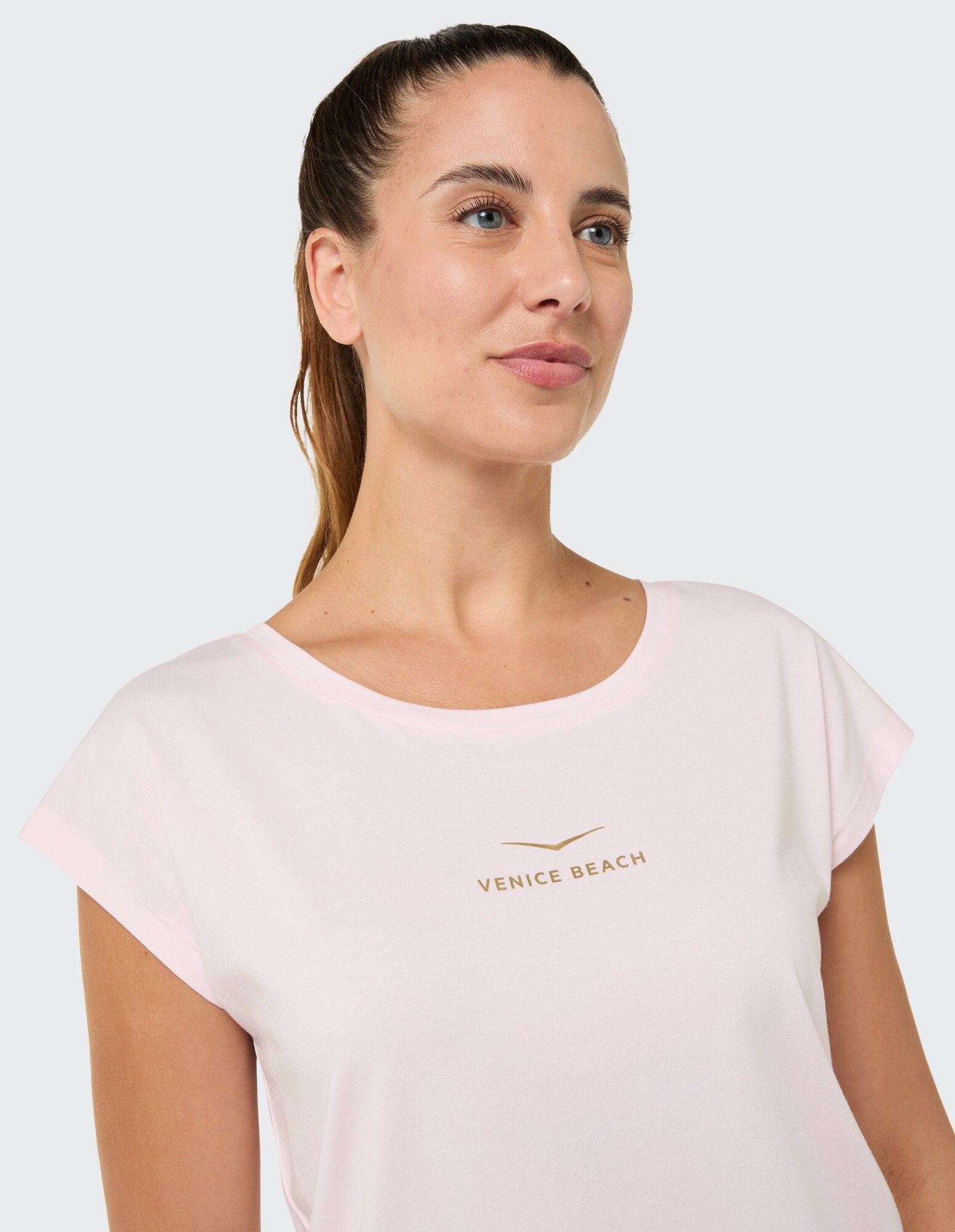 Frau trägt ein hellrosa T-Shirt mit „Venice Beach“-Logo im lässigen Stil.