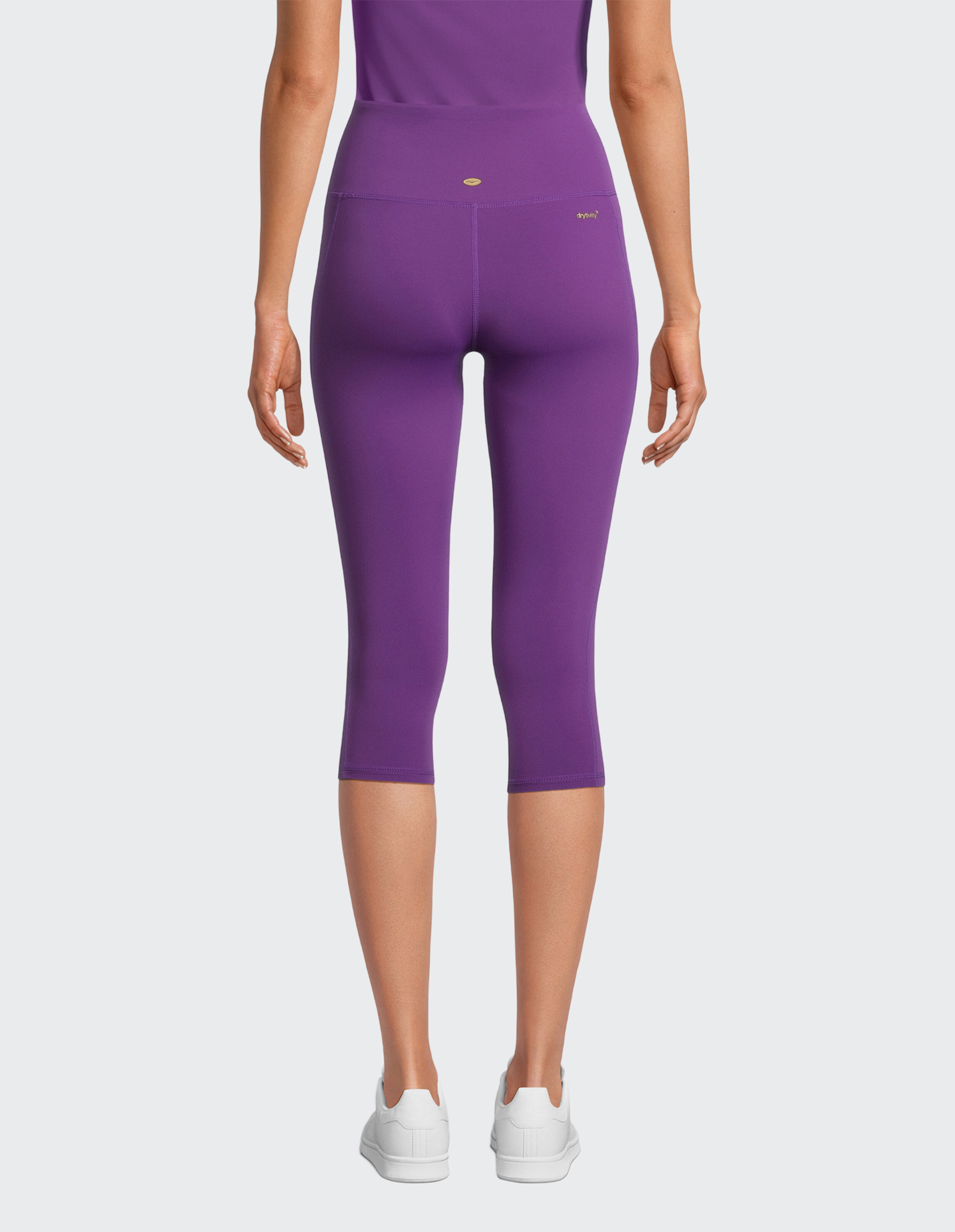 Rückansicht einer Frau in lila Capri-Leggings und weißen Turnschuhen.