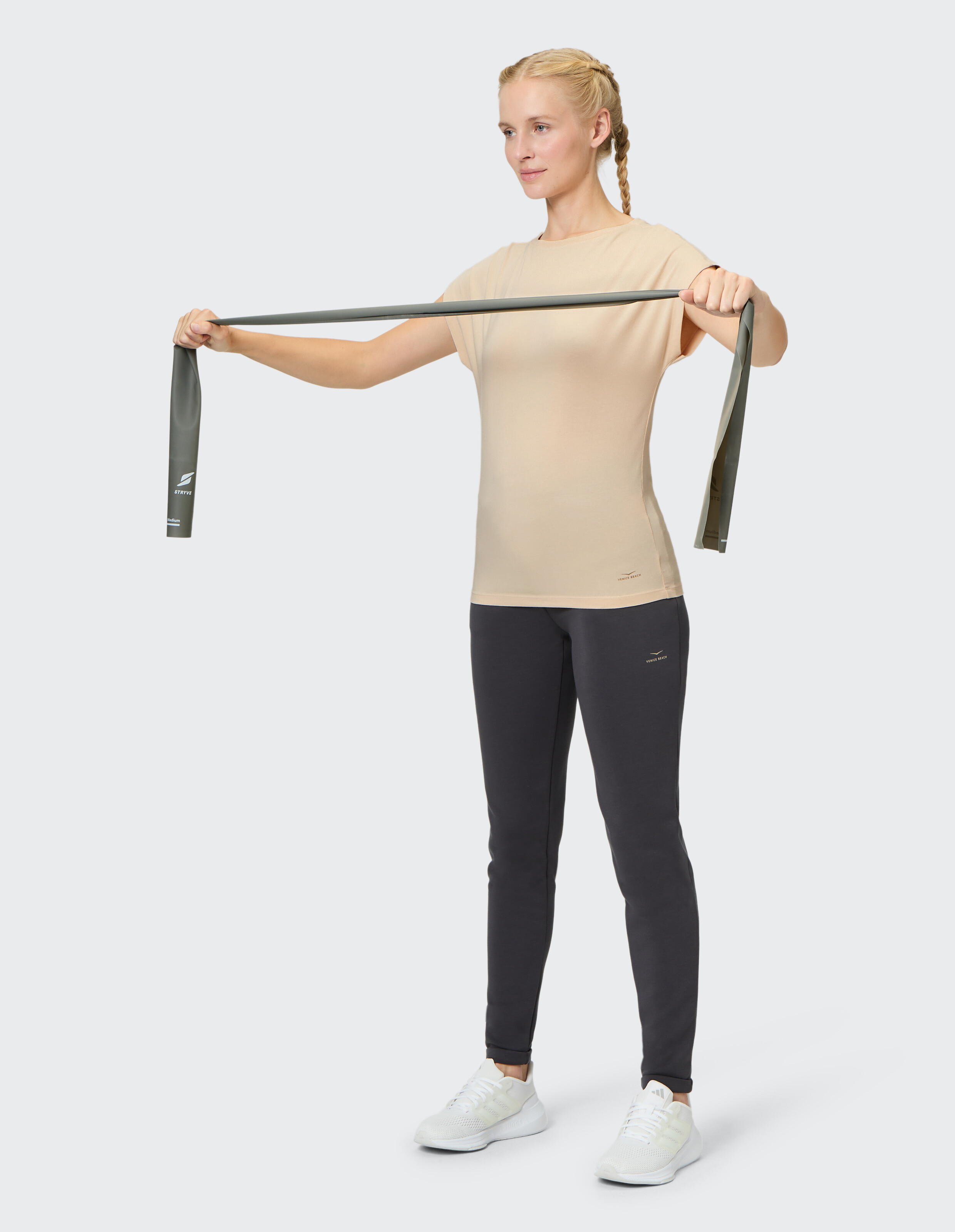 Frau im beigefarbenen Venice Beach Kurzarmshirt Yvi trainiert mit einem Widerstandsband.